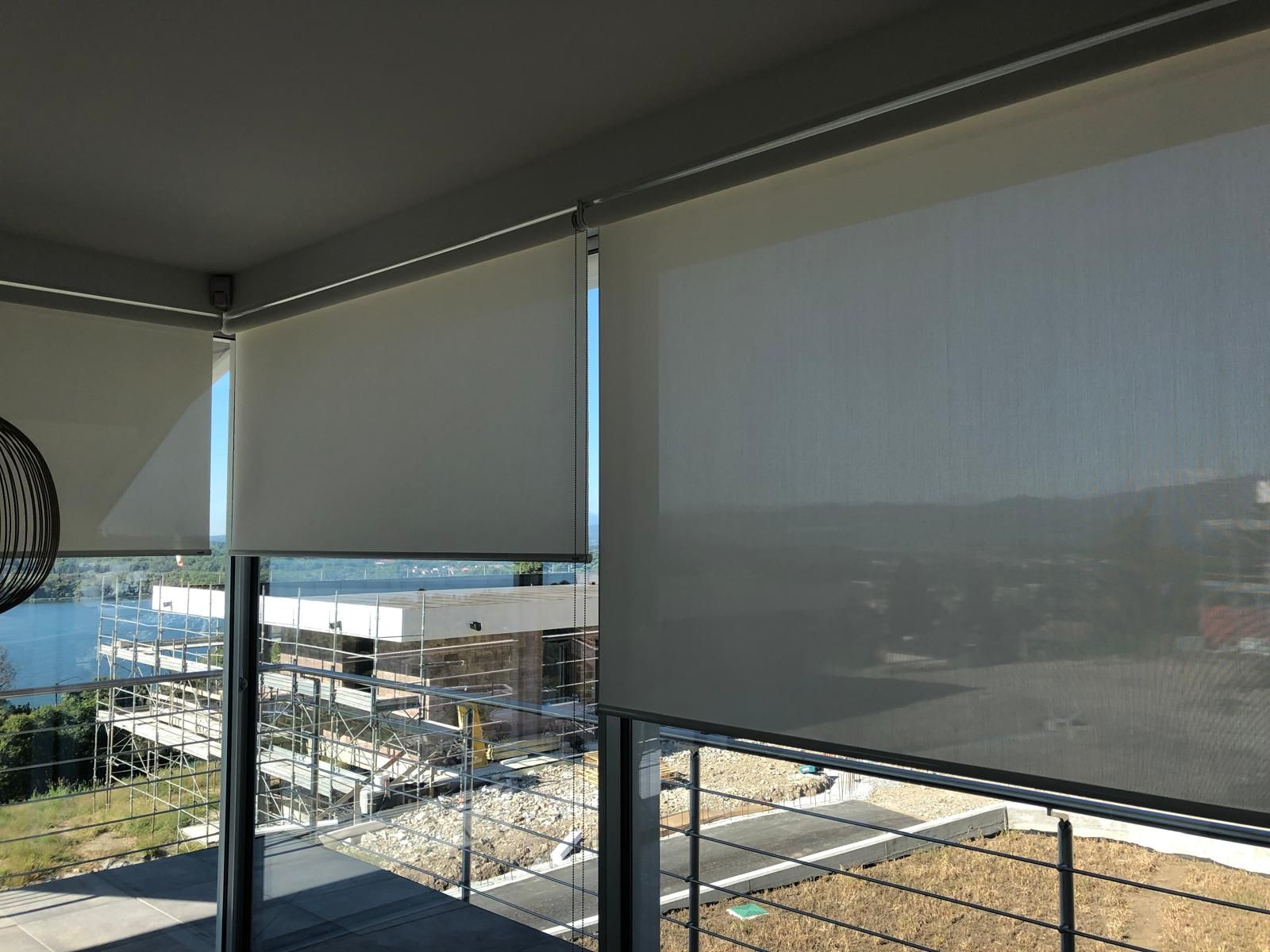 Tende a rullo installate su una finestra che si affaccia su un cantiere e su uno specchio d'acqua.