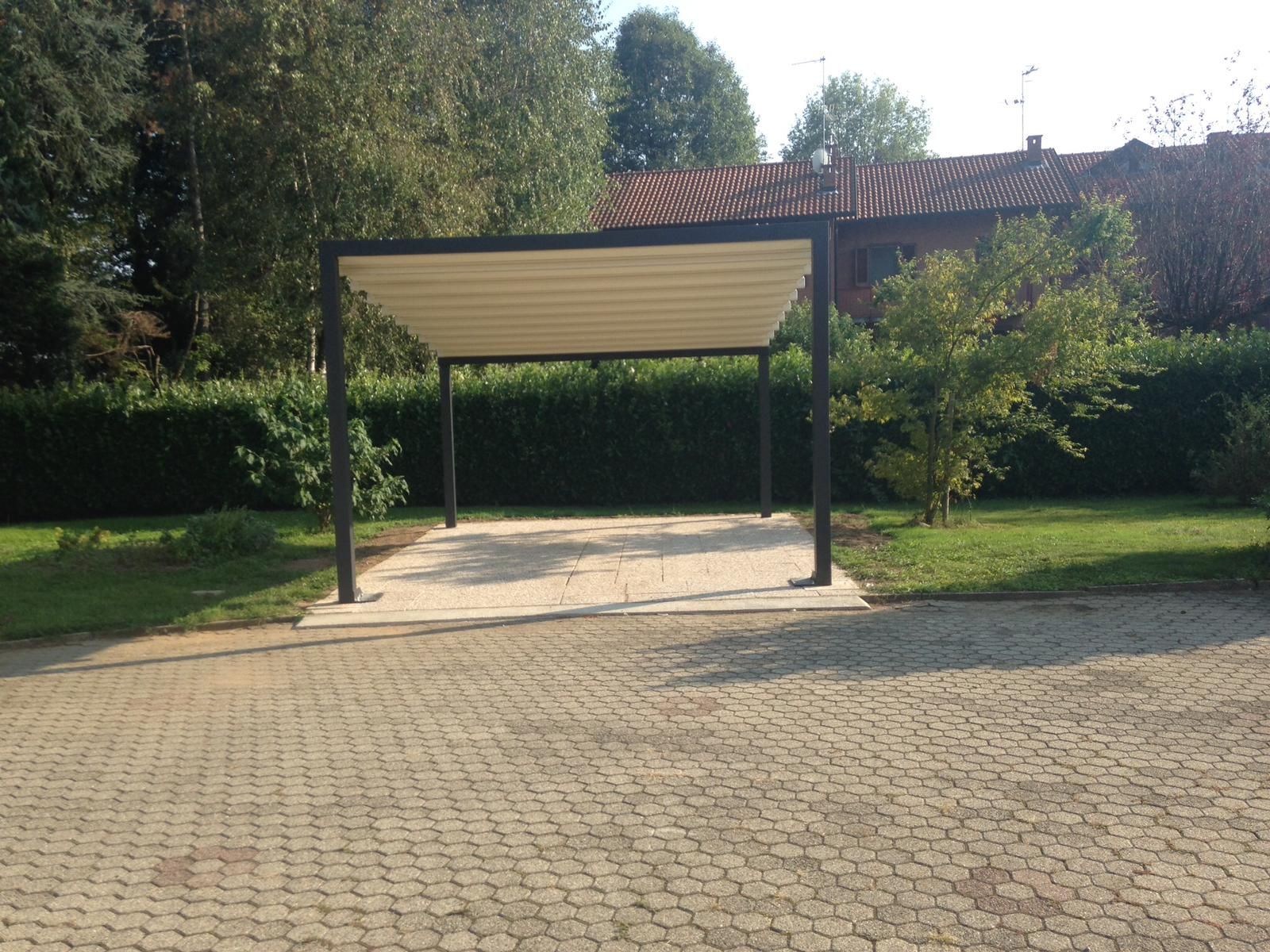 Una moderna pergola con struttura scura e tettoia retrattile di colore chiaro, installata sopra un patio pavimentato in un giardino erboso.