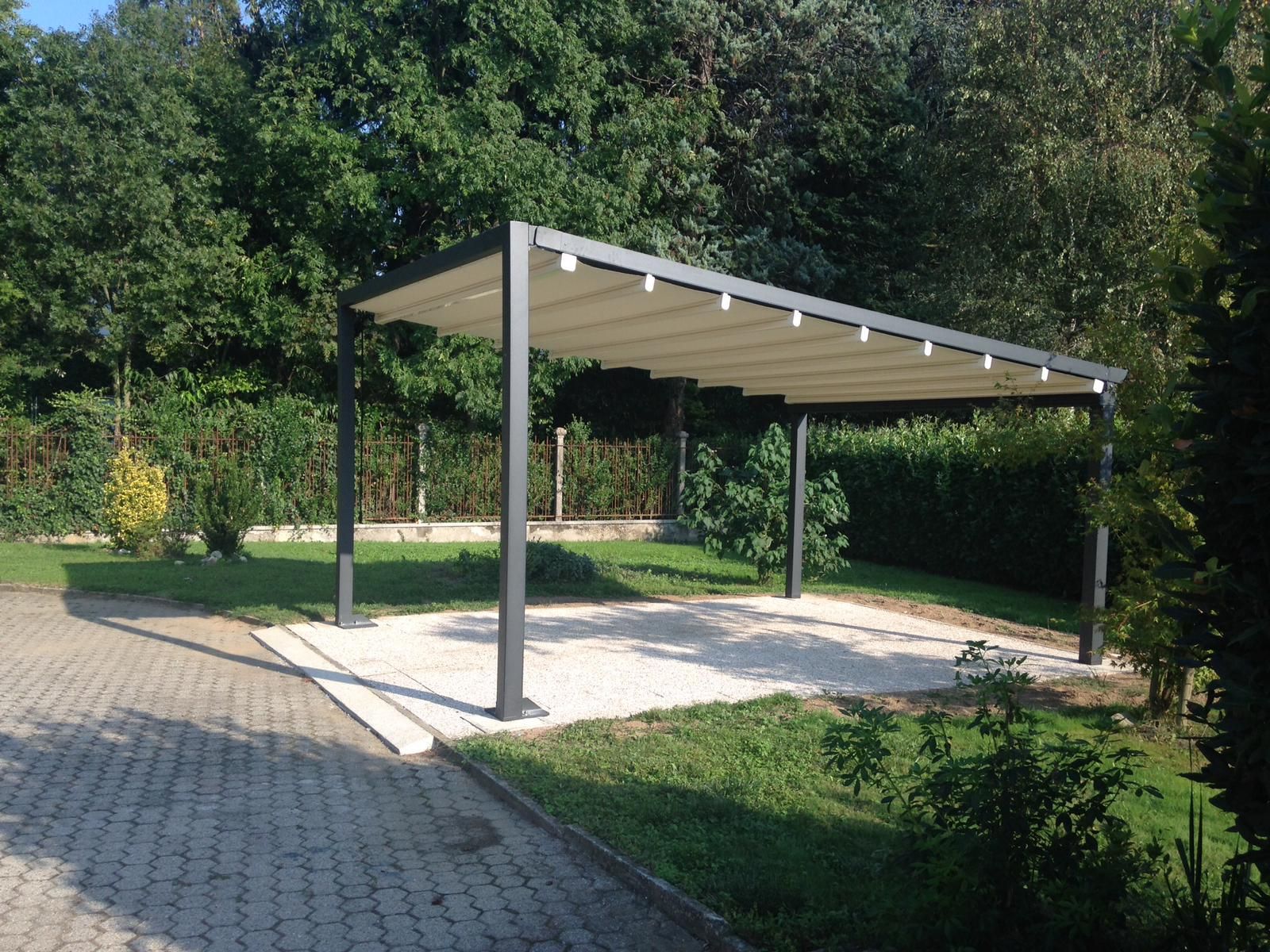 In un soleggiato cortile sul retro, una pergola in metallo grigio con tetto retrattile in tessuto beige si erge su una zona ghiaiosa.