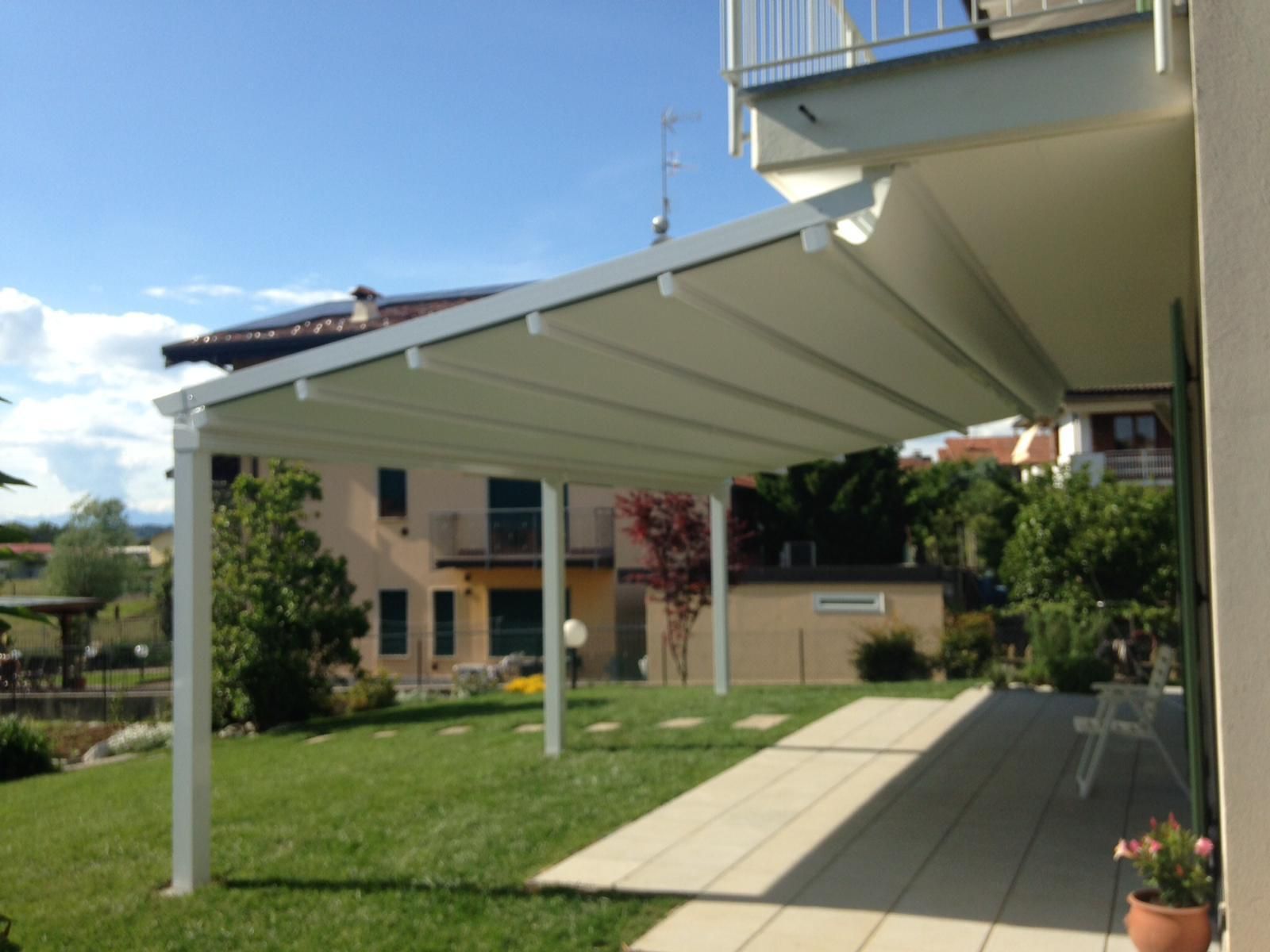 Una tenda da sole retrattile bianca si estendeva su una terrazza pavimentata, affacciata su un prato verde e su un'abitazione.