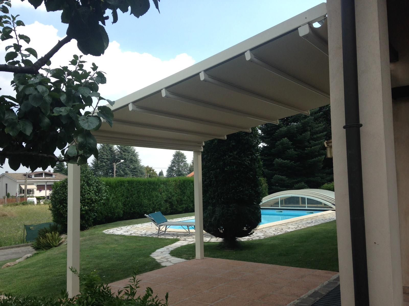 Nelle giornate di sole, un patio coperto si affaccia su un giardino con piscina, prato verde e siepe.