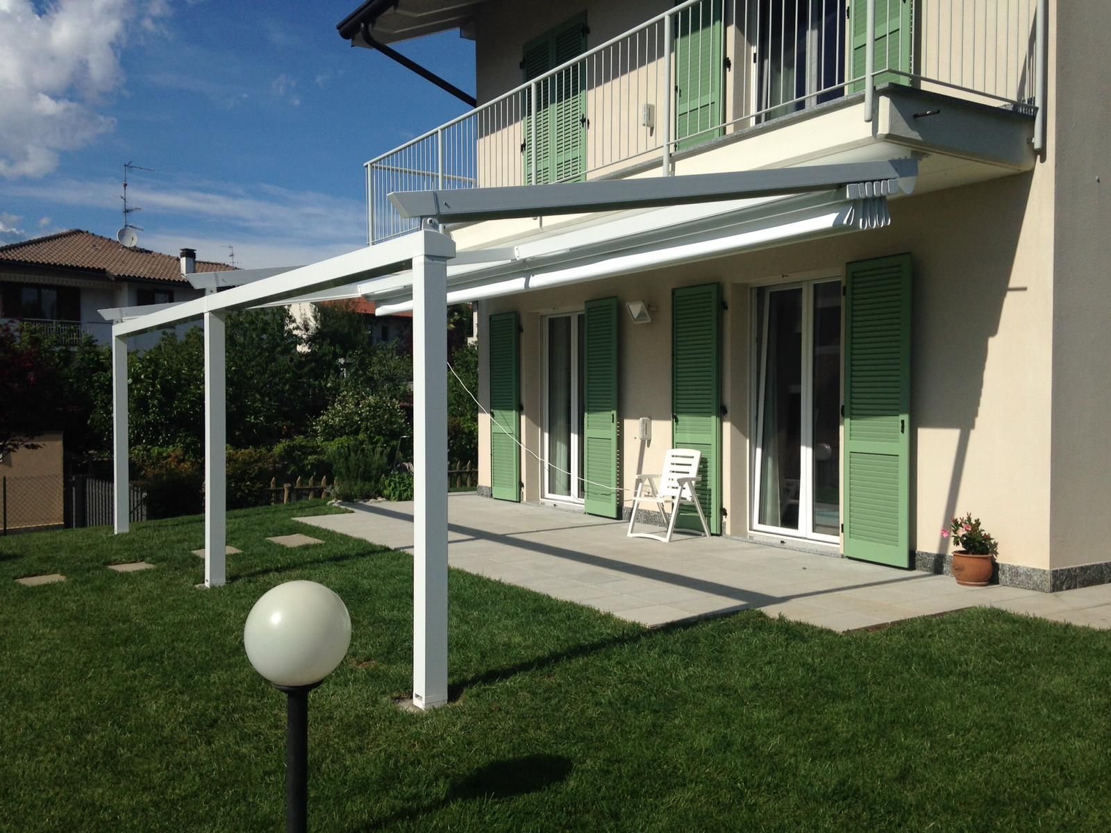 In una giornata di sole, una pergola bianca si estende da una casa con persiane verdi sopra un patio.