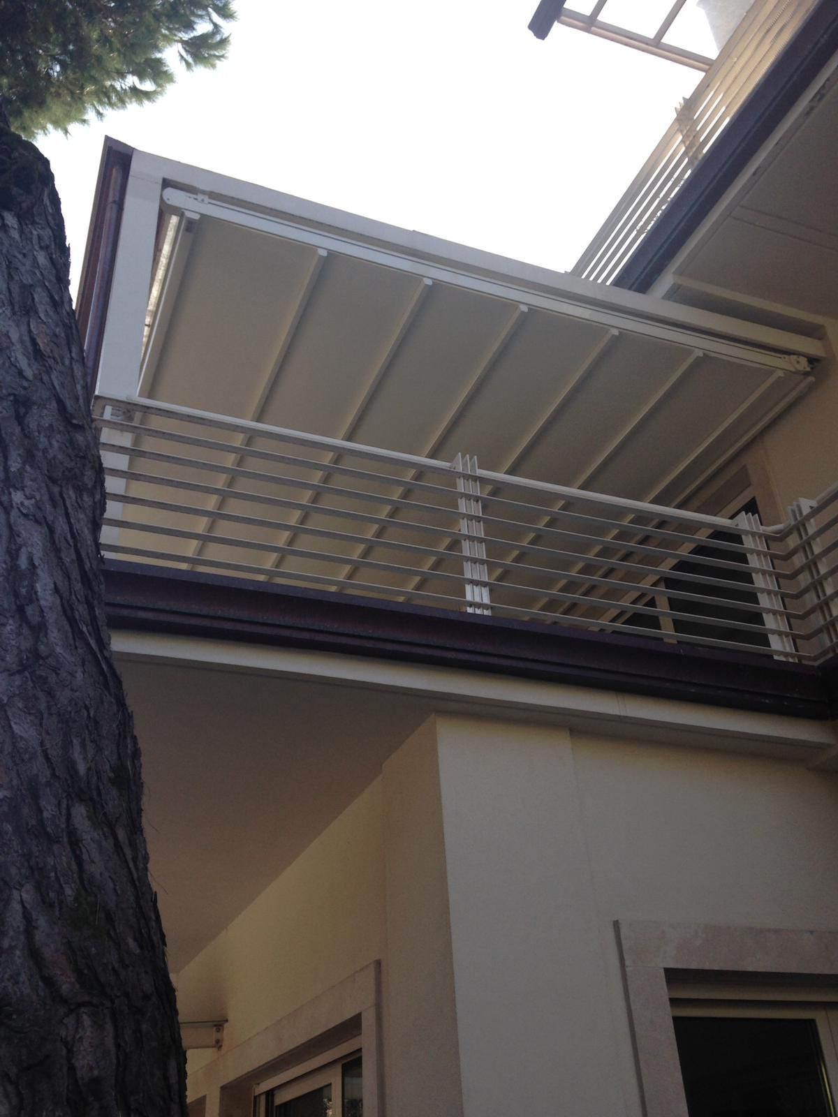 Una tenda a pergola retrattile di colore chiaro si estendeva sopra un balcone con una ringhiera a griglia bianca sul lato di un edificio.
