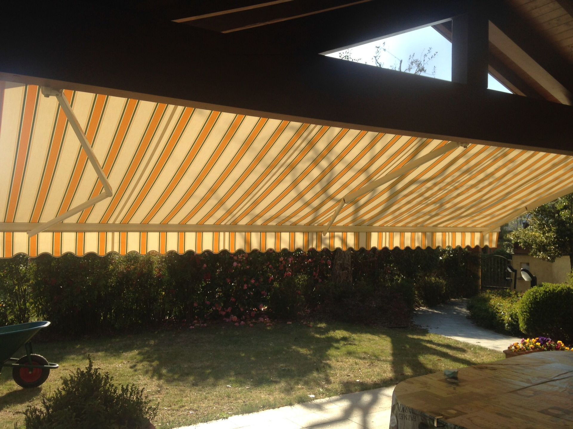 Una tenda da sole retrattile a strisce gialle e bianche si estendeva sopra un patio sul retro di una casa, con prato e siepe.