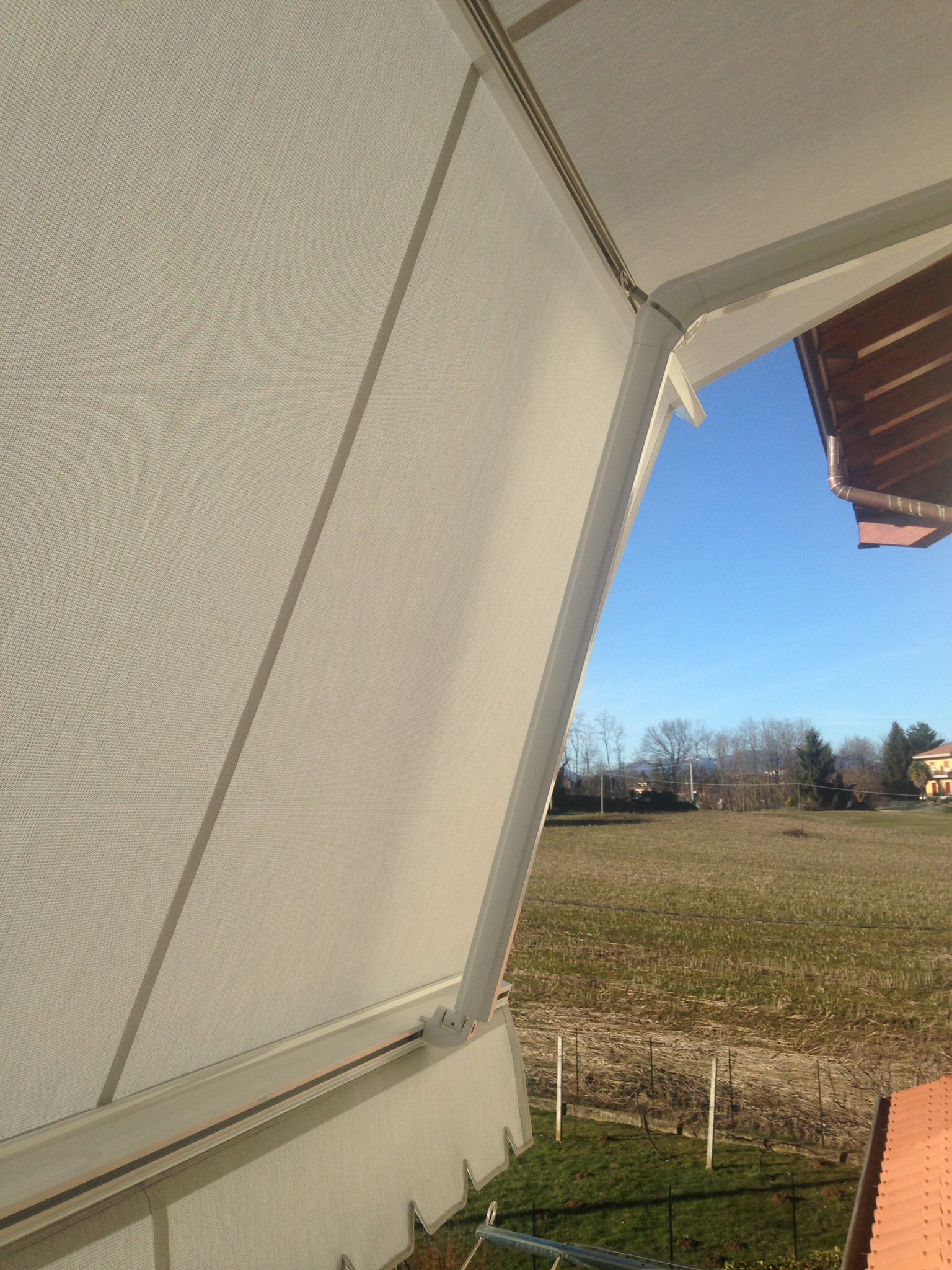 Una schermatura per la privacy di colore chiaro e dalla forma angolata, che si affaccia su un campo in campagna sotto un cielo azzurro e limpido.