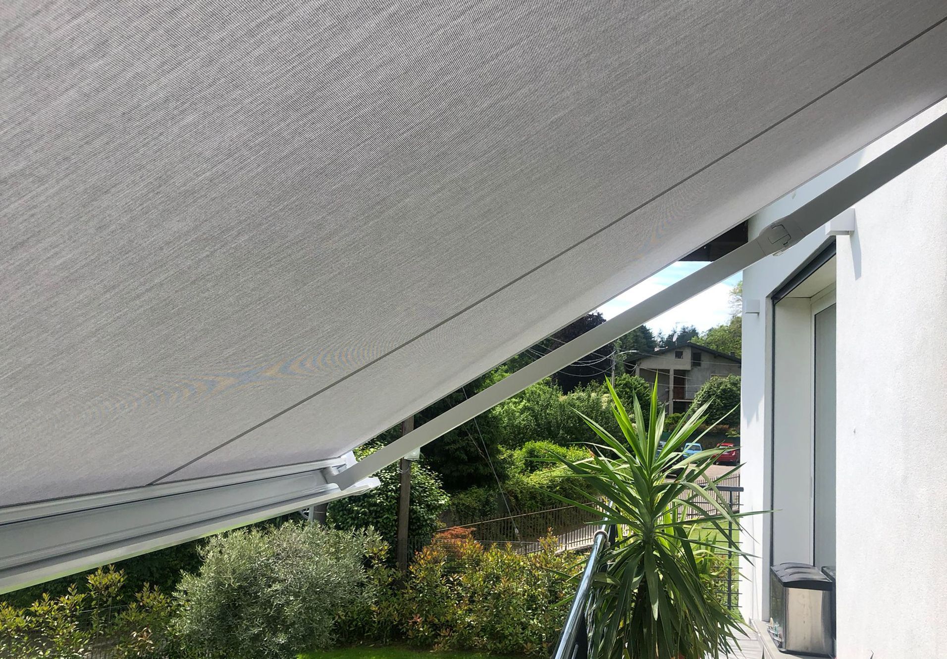 Una tenda da sole in tessuto chiaro si estende da una parete bianca, ombreggiando un patio con sullo sfondo una rigogliosa vegetazione verde.