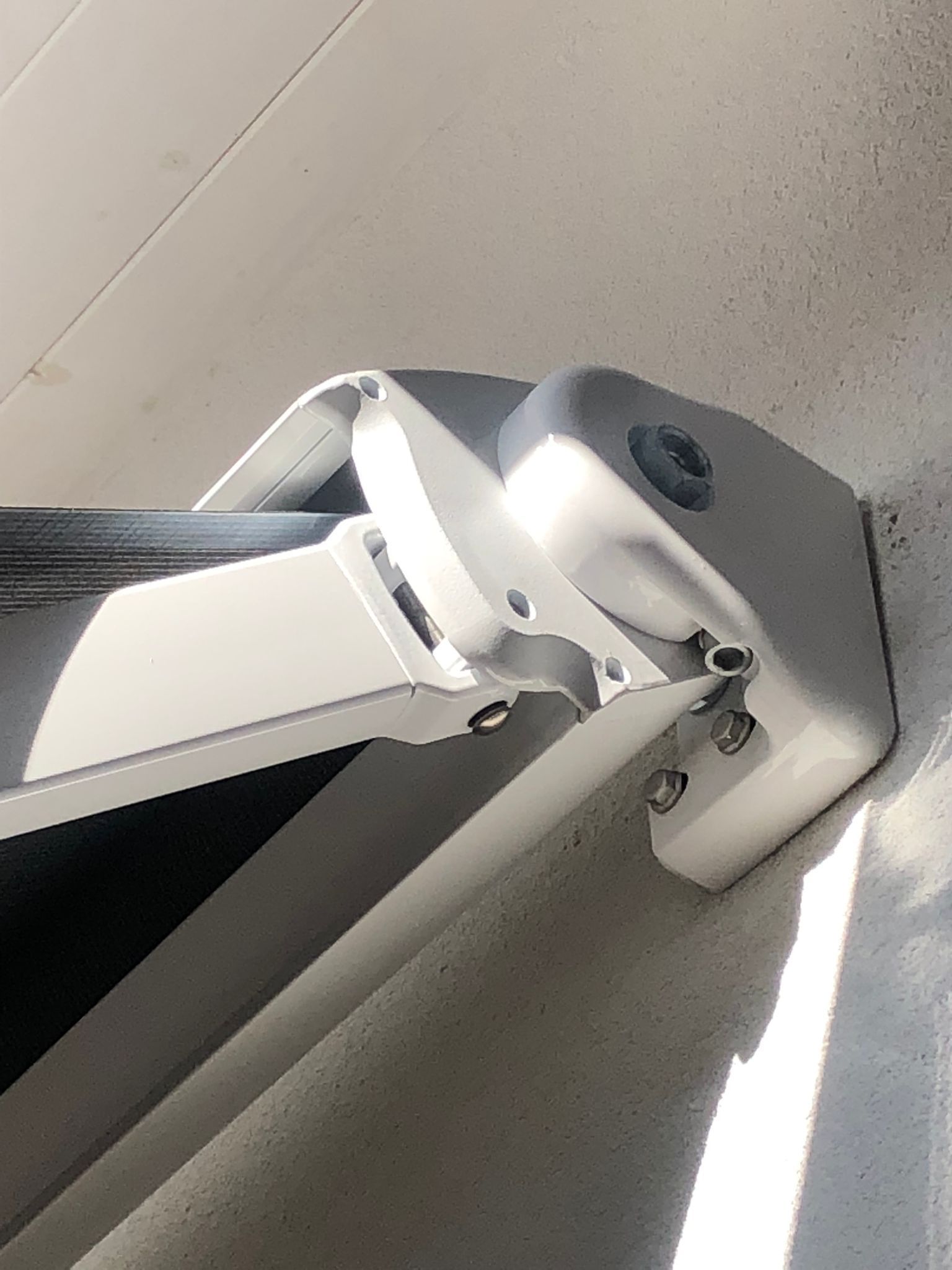 Primo piano di una staffa di montaggio in metallo bianco rotta, destinata a una tenda da sole retrattile per esterni fissata a una parete.