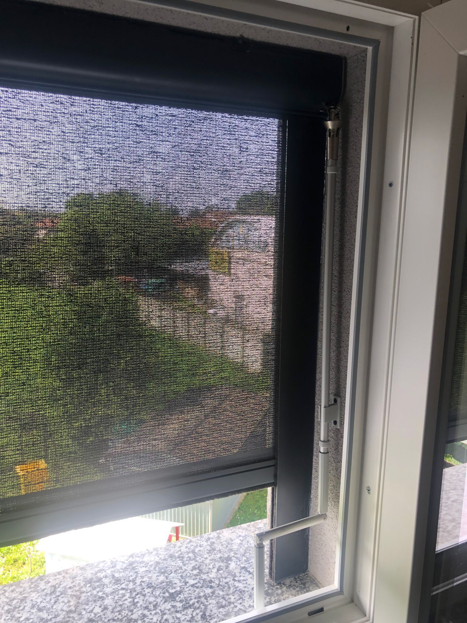 Una tenda a rullo scura è parzialmente abbassata su una finestra con una piccola porticina bianca per animali domestici installata nell'angolo inferiore.