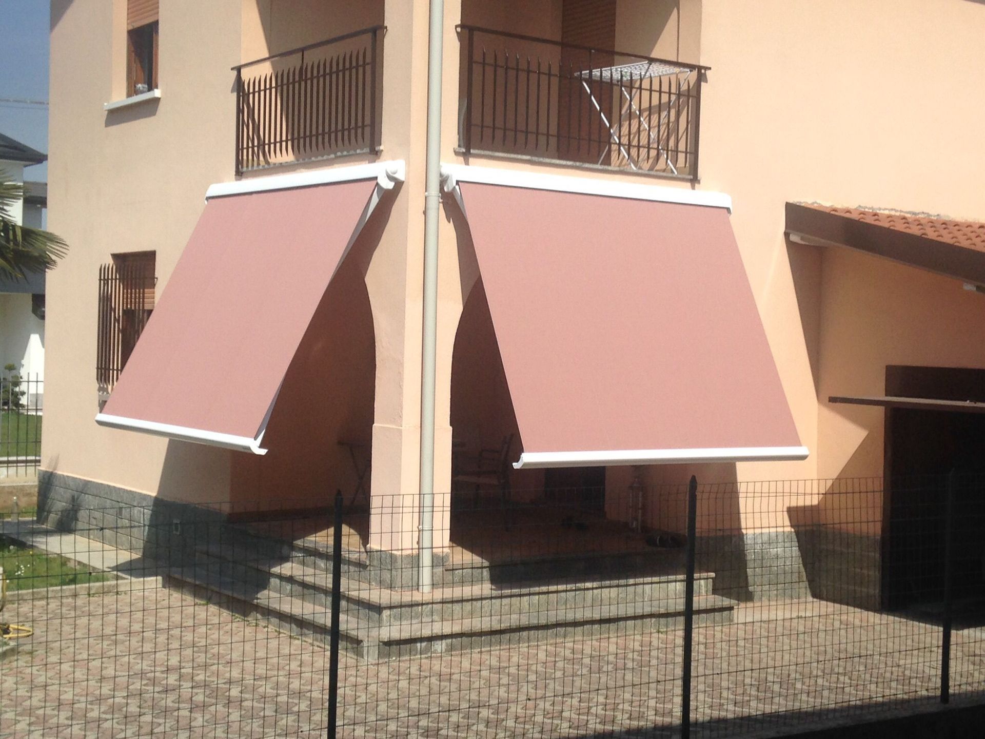 Una casa a due piani color arancio chiaro, con due tende da sole retrattili rosa abbinate che si estendono su un patio d'angolo.