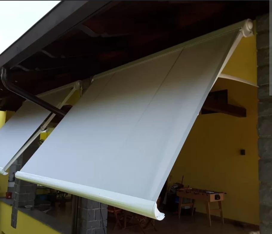 Due tende da sole beige per esterni si estendono verso il basso da una sporgenza del tetto per fornire ombra a una zona patio.