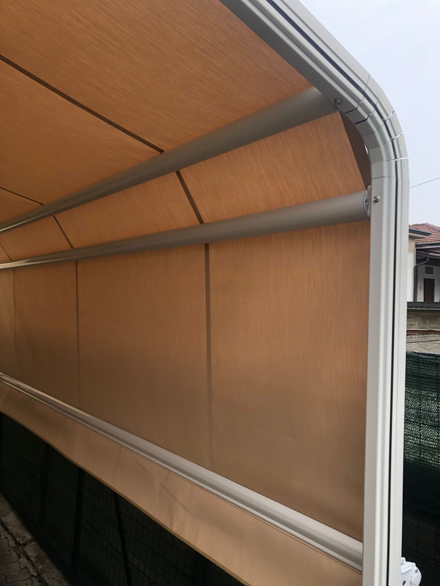 Una tenda da sole retrattile per esterni, di colore beige, con struttura in metallo bianco, che si estende sopra un patio o una terrazza.