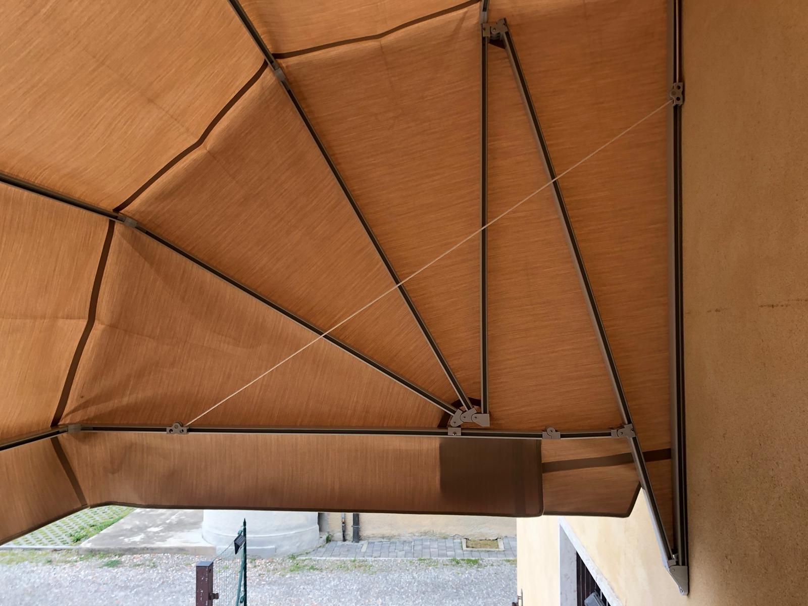 Una tenda da sole in tela color beige con struttura metallica geometrica fissata alla parete di un edificio.