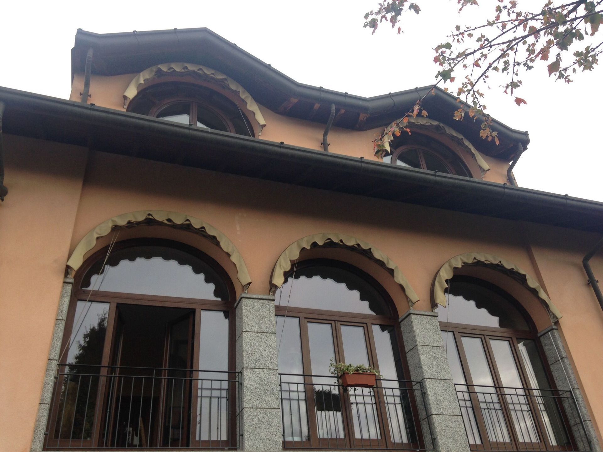 Facciata della casa color salmone con tre finestre ad arco sul balcone e due abbaini più piccoli con cornici decorative.