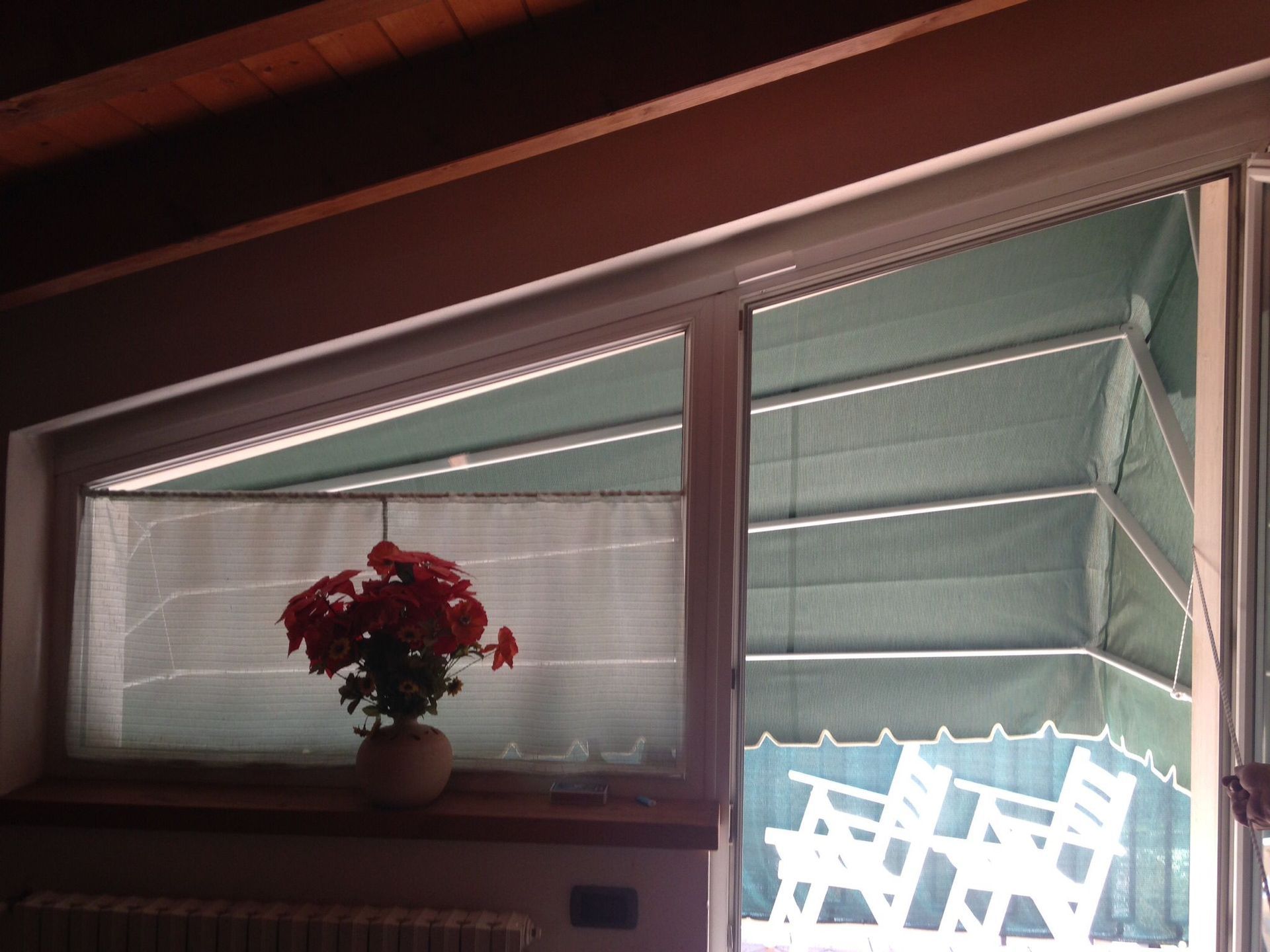 Un mazzo di fiori rossi è appoggiato sul davanzale di una finestra accanto a una porta scorrevole, mentre sul patio esterno si intravedono delle sedie bianche.