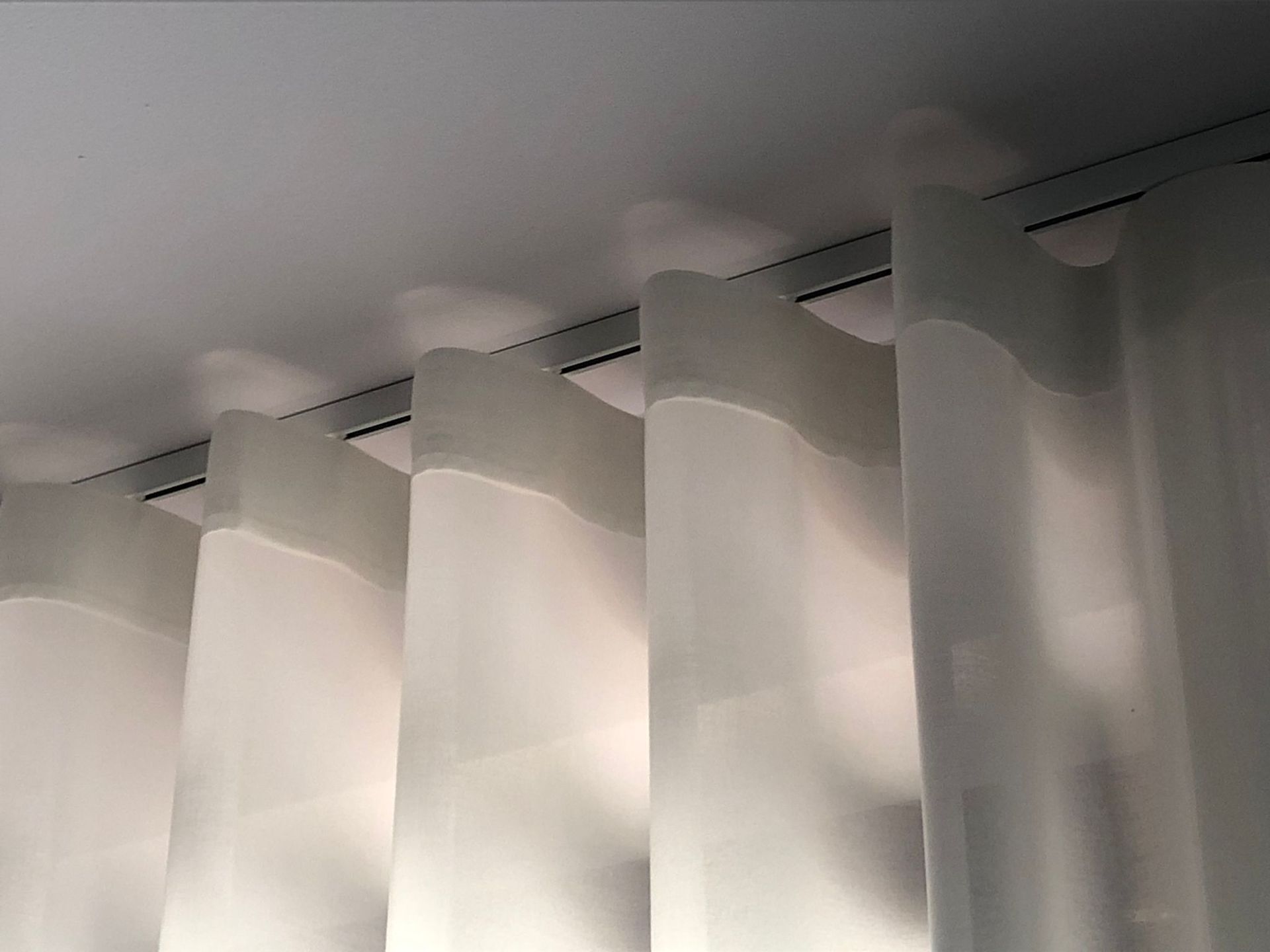 Tende bianche a pieghe a S o a onda, appese a un binario montato a soffitto.