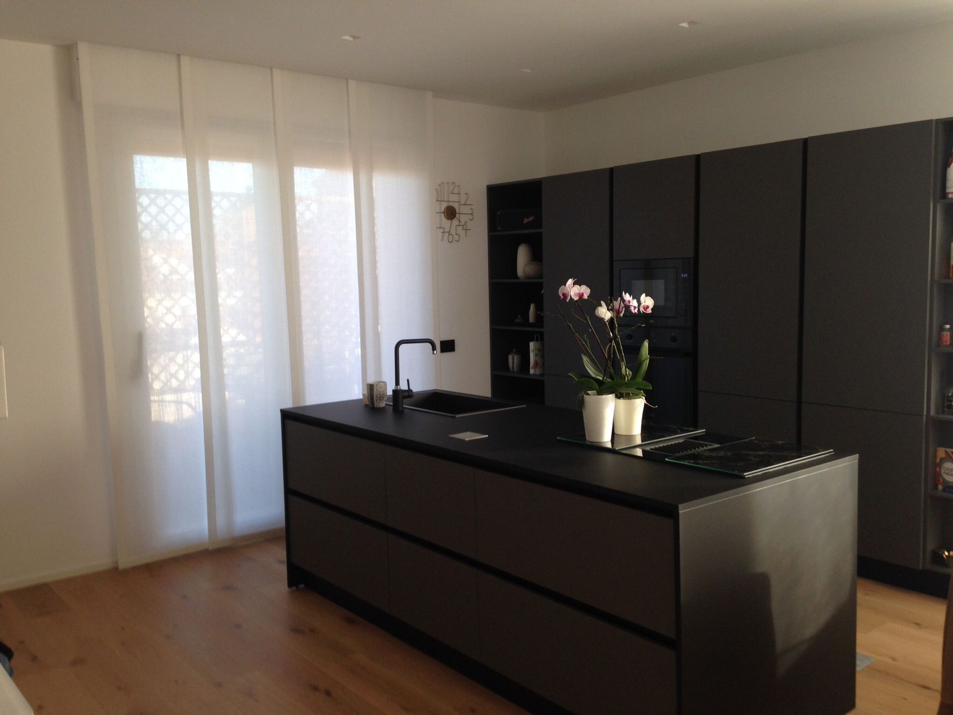 Una cucina moderna caratterizzata da un'isola scura con lavello, piano cottura e orchidee bianche in vaso, il tutto incorniciato da mobili scuri.
