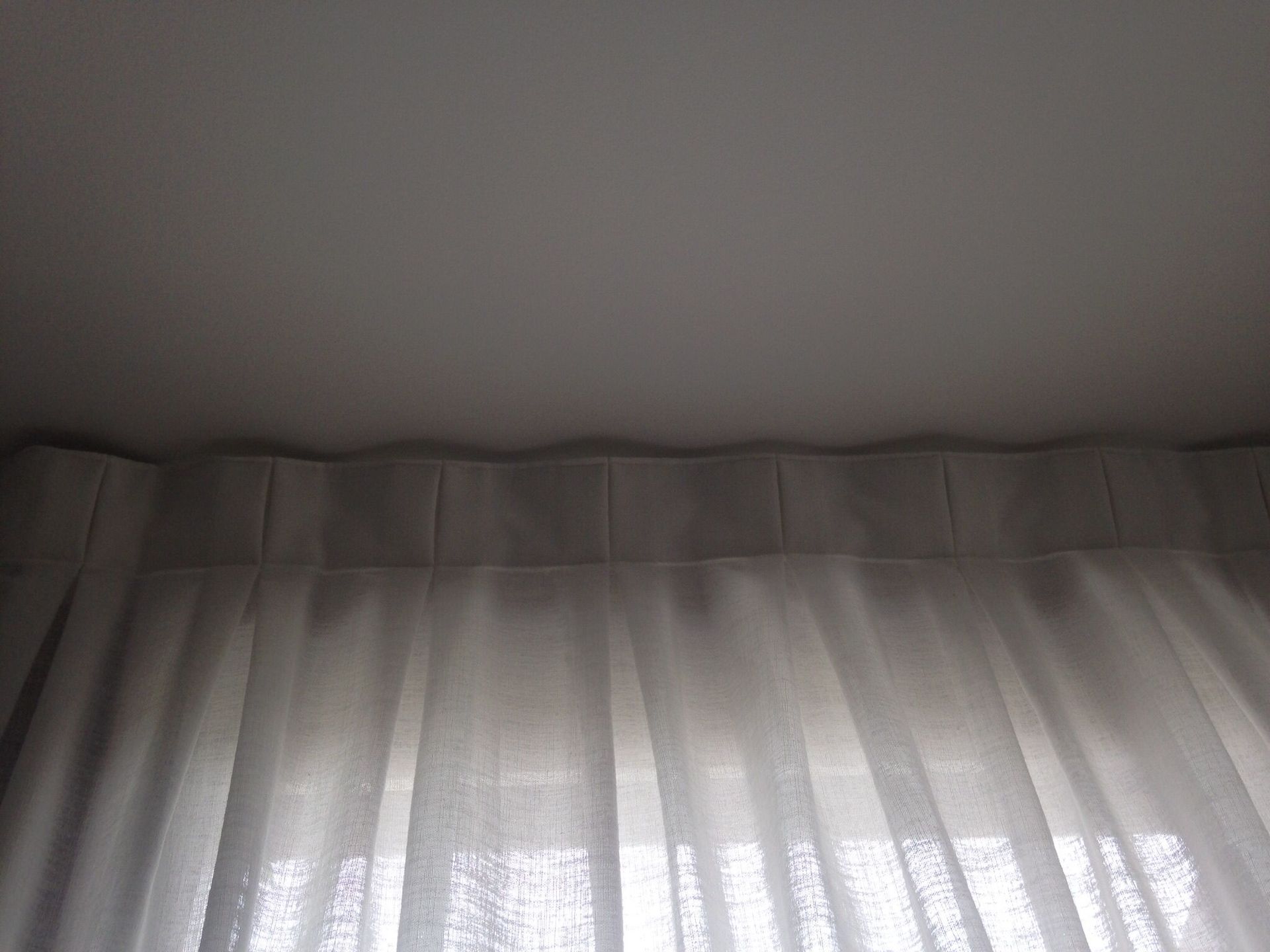 Tende bianche con una parte superiore plissettata, appese a un binario montato a soffitto.