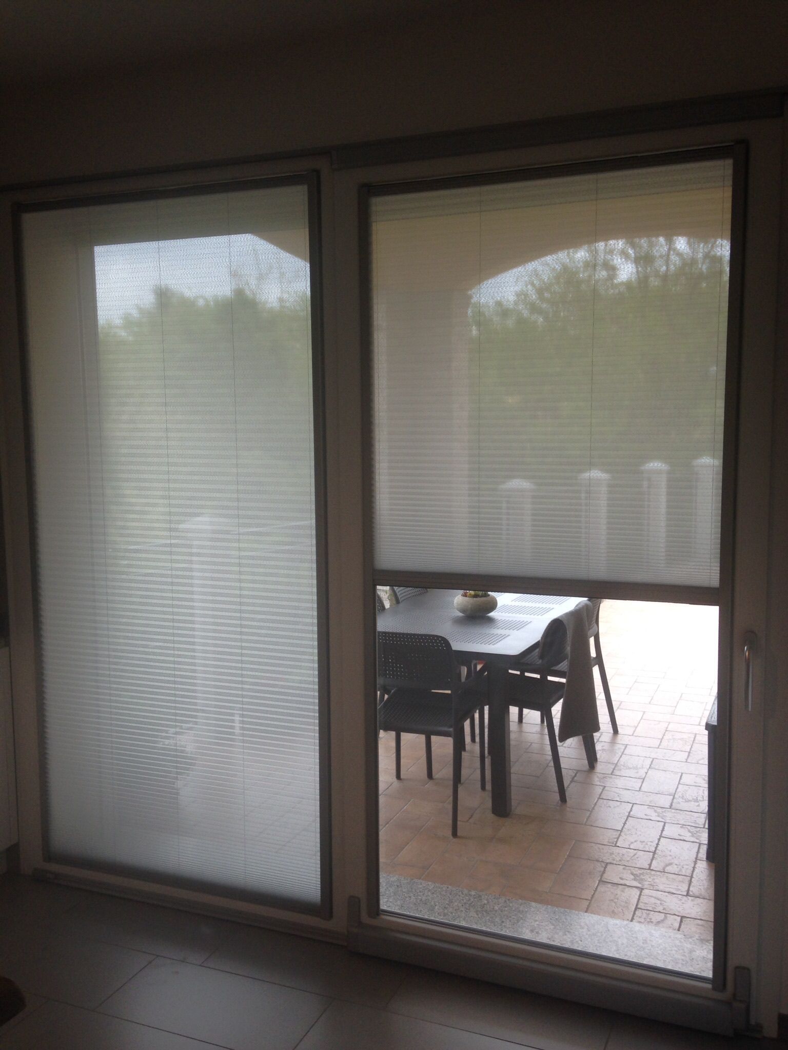 Una vista attraverso porte scorrevoli in vetro, con un pannello chiuso e l'altro semiaperto, che mostra un set da pranzo da patio all'esterno.