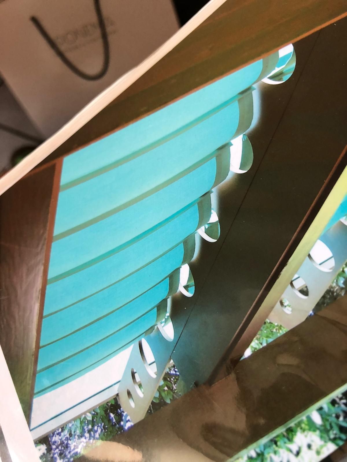 Vista verticale di una struttura con pannelli azzurri e un telaio metallico con aperture circolari, sullo sfondo di una vegetazione.