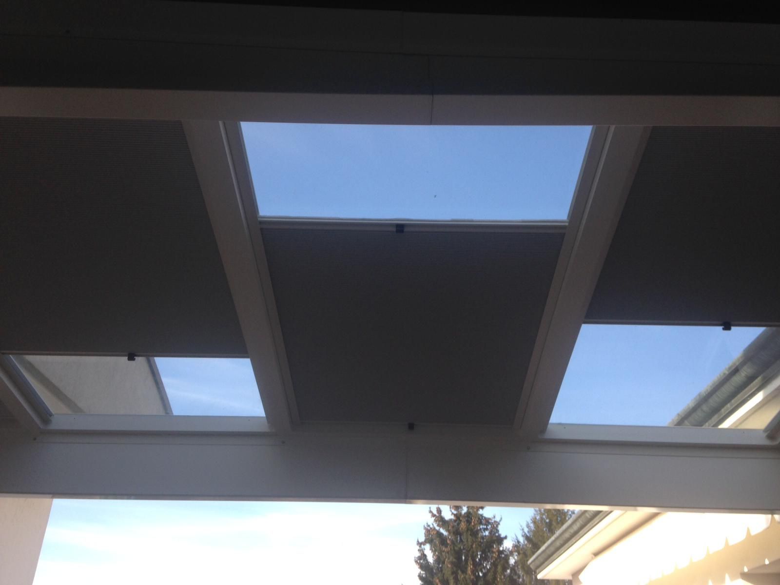 Tre lucernari incastonati in una struttura a soffitto bianca, uno completamente aperto e due parzialmente coperti da tende grigio scuro.