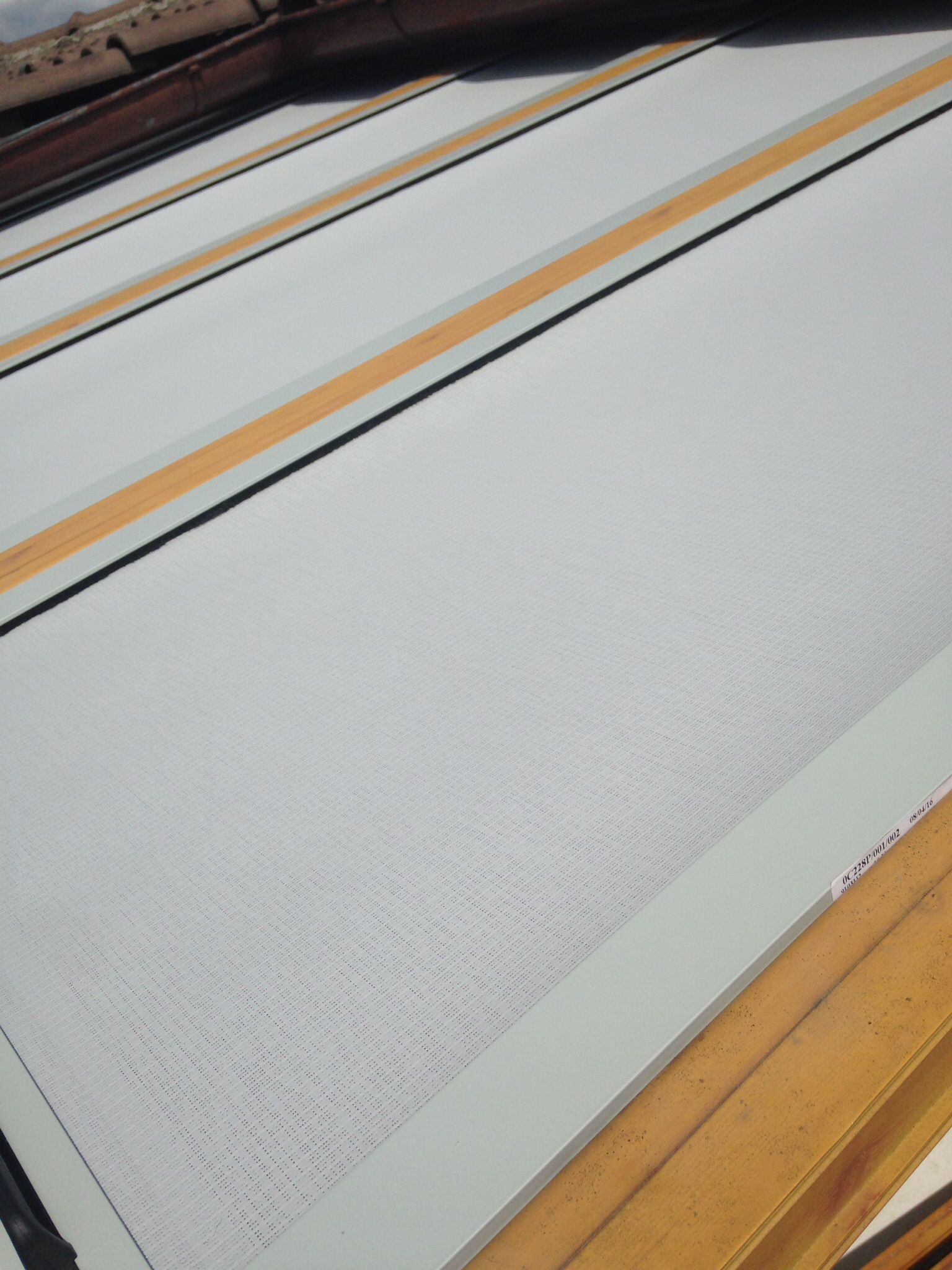 Una schermatura o un parasole bianco e strutturato, installato su un telaio di legno con strisce orizzontali color cuoio.