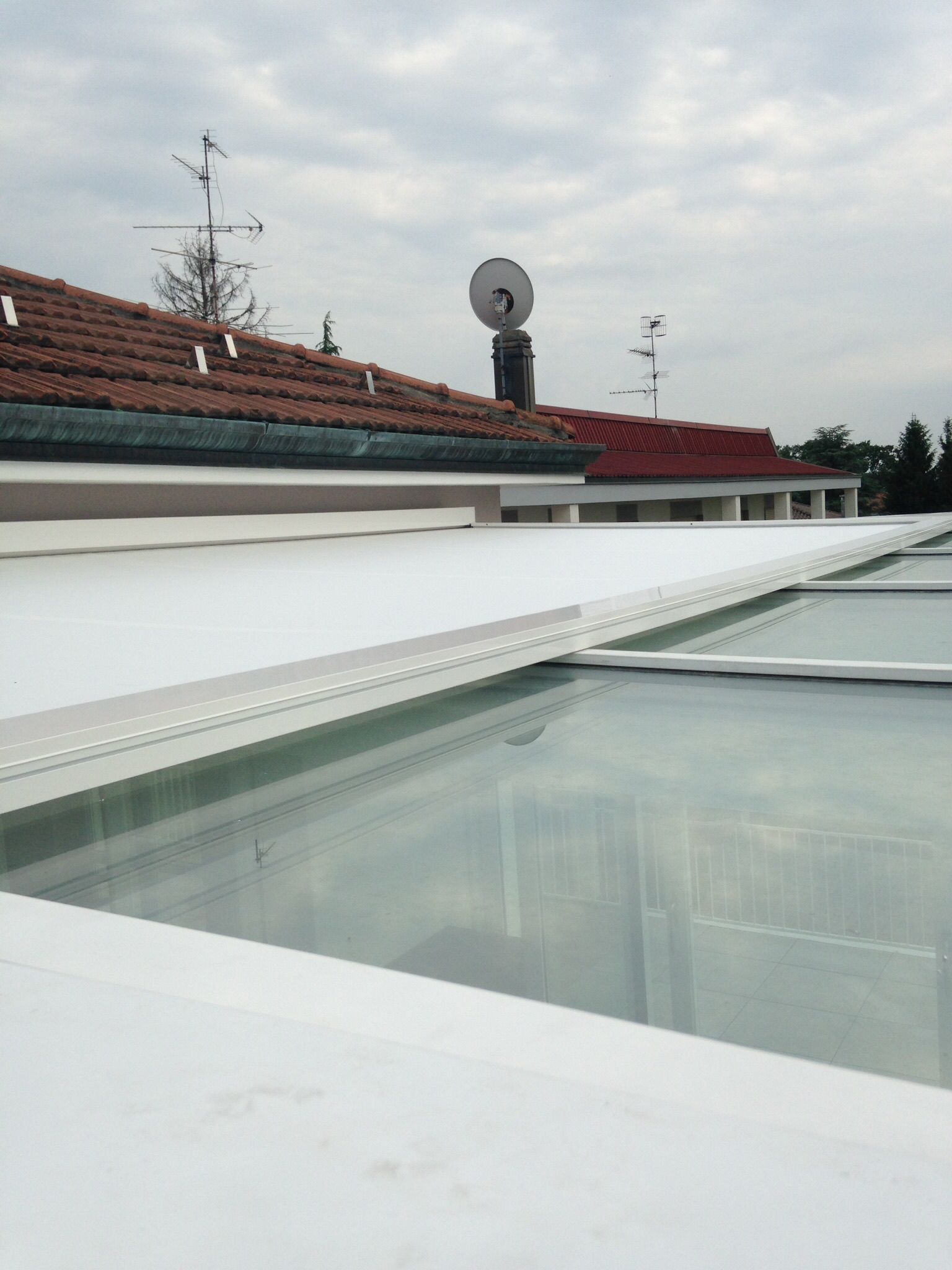 Un lucernario in vetro con una tenda da sole retrattile bianca parzialmente estesa su un tetto sotto un cielo nuvoloso.