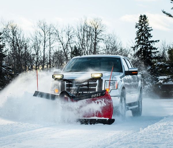 Pickup truck pushing snow with a red plow on a snowy road, headlights on