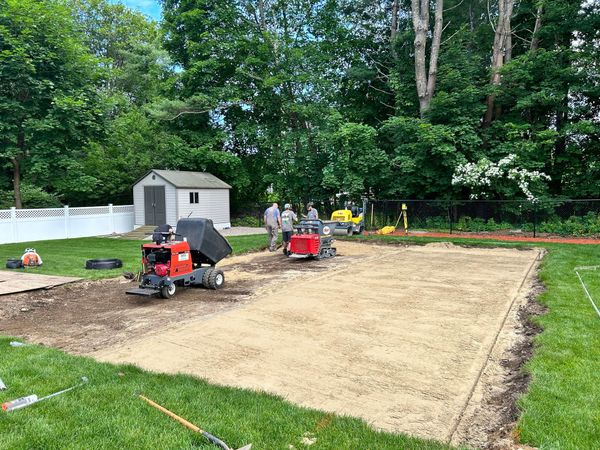 Two red skid-steer loaders grading a backyard lawn beside a shed and trees