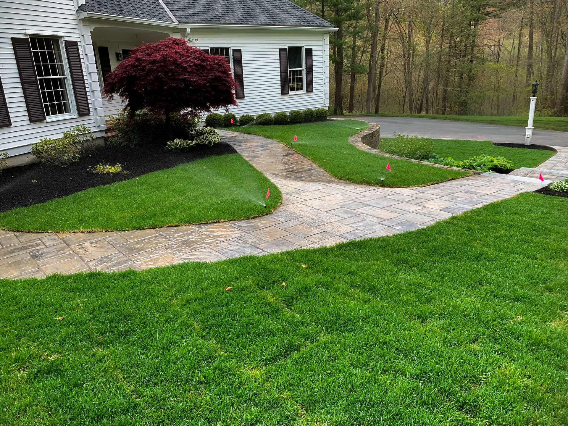 Curved stone walkway through a green lawn beside a white house and burgundy shrubbery