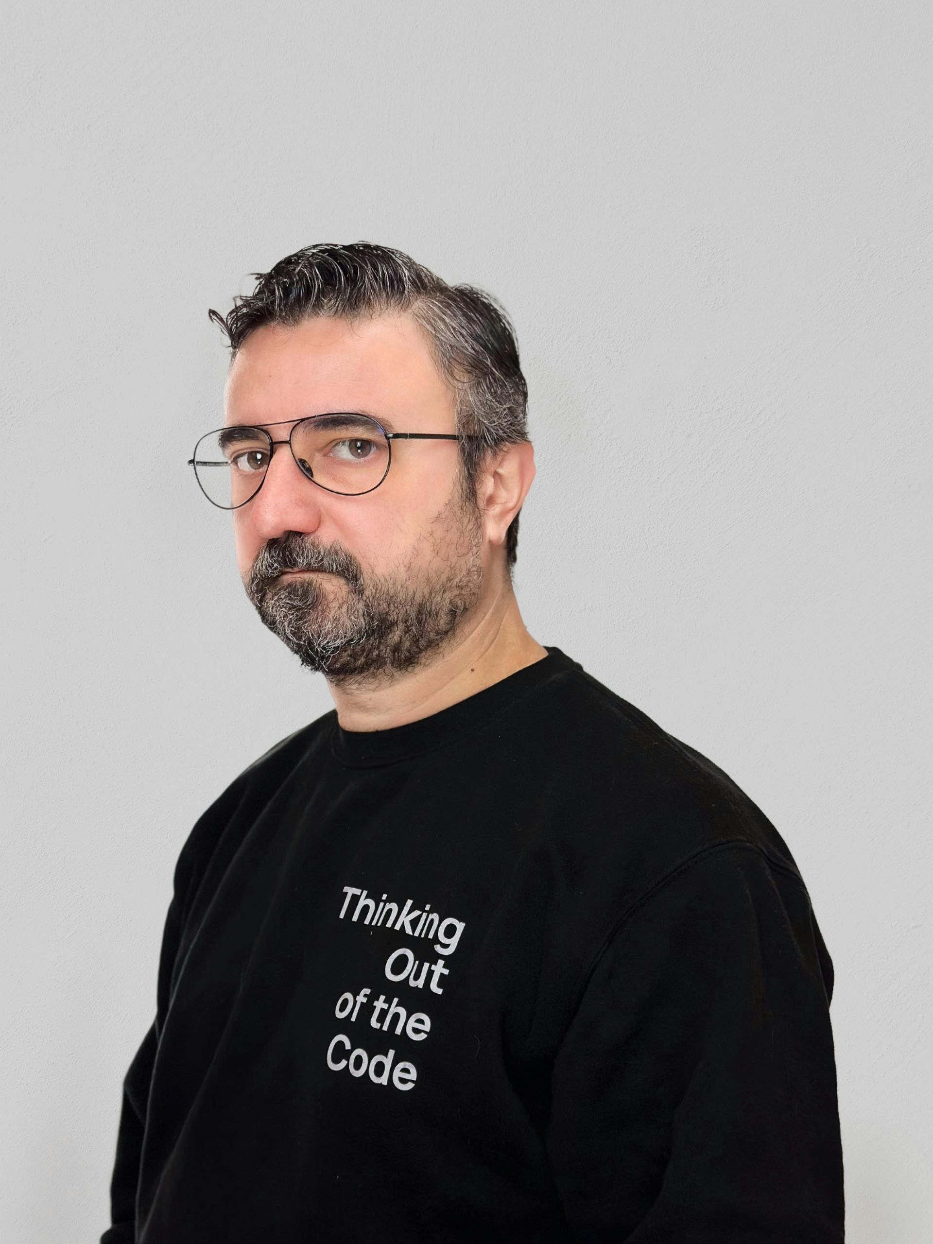 Man with glasses and a beard in a black T-shirt, standing against a light gray background.