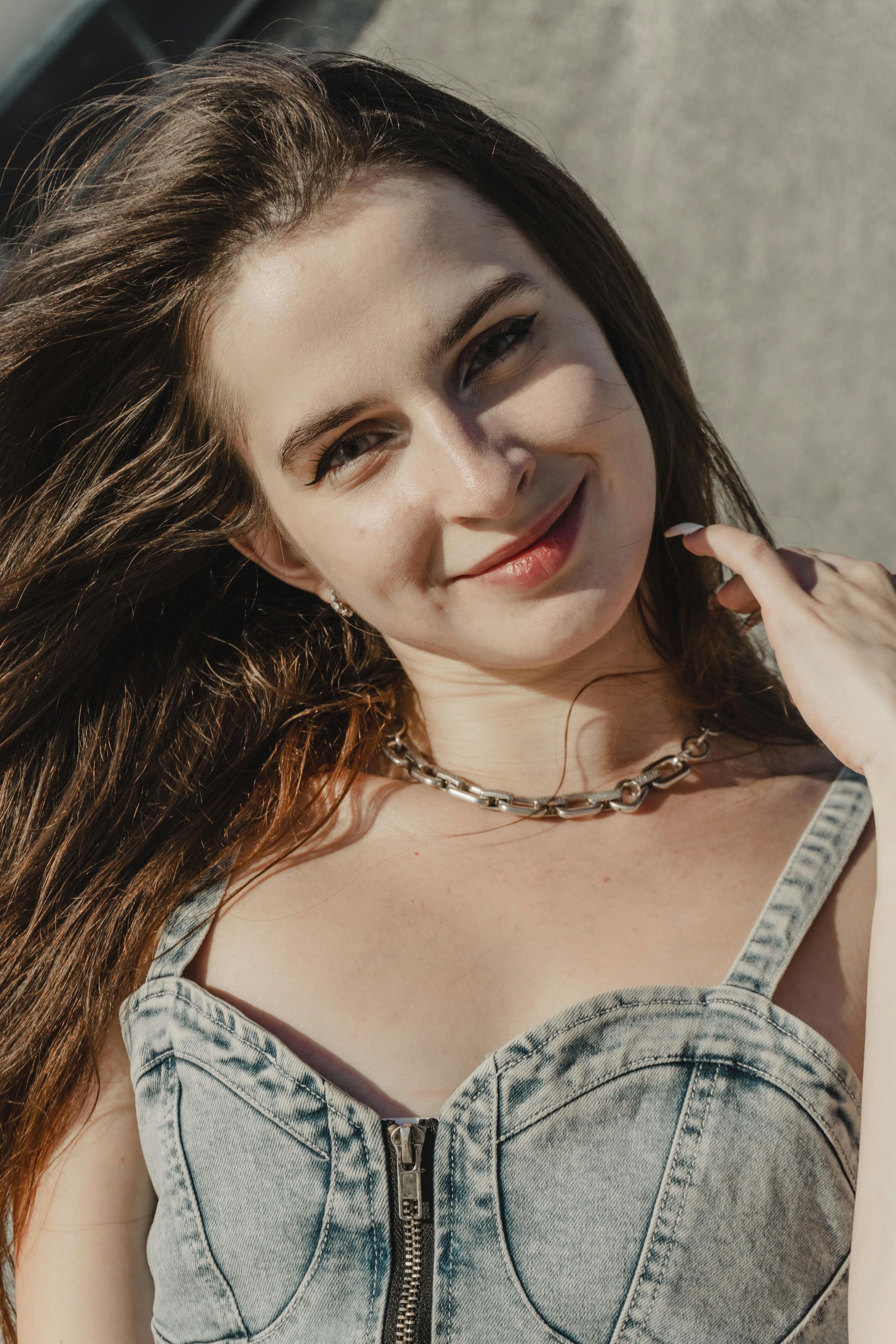Woman smiling in a gray denim corset top, standing in sunlight with windblown hair.