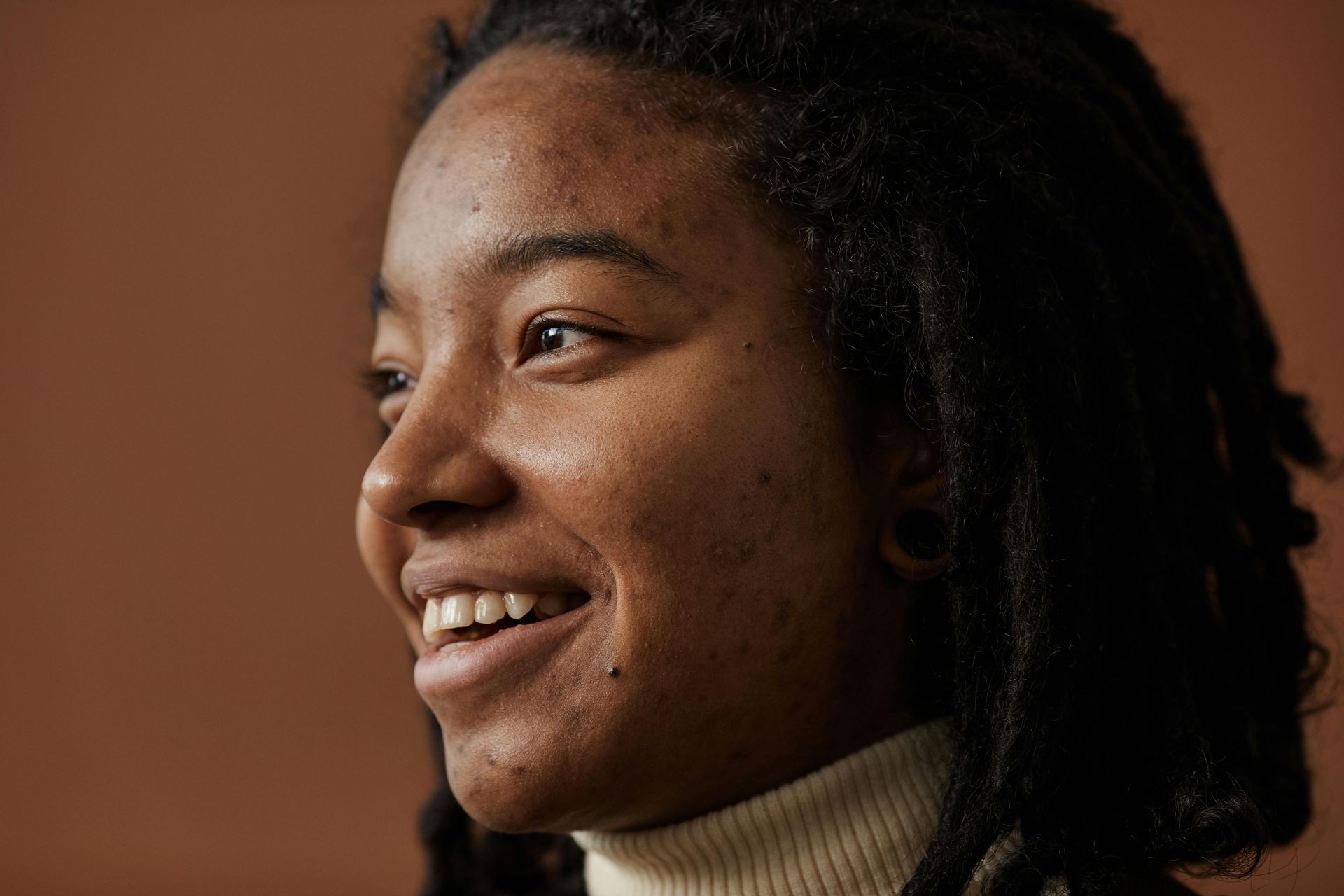 Close-up of a smiling person in profile against a warm brown background