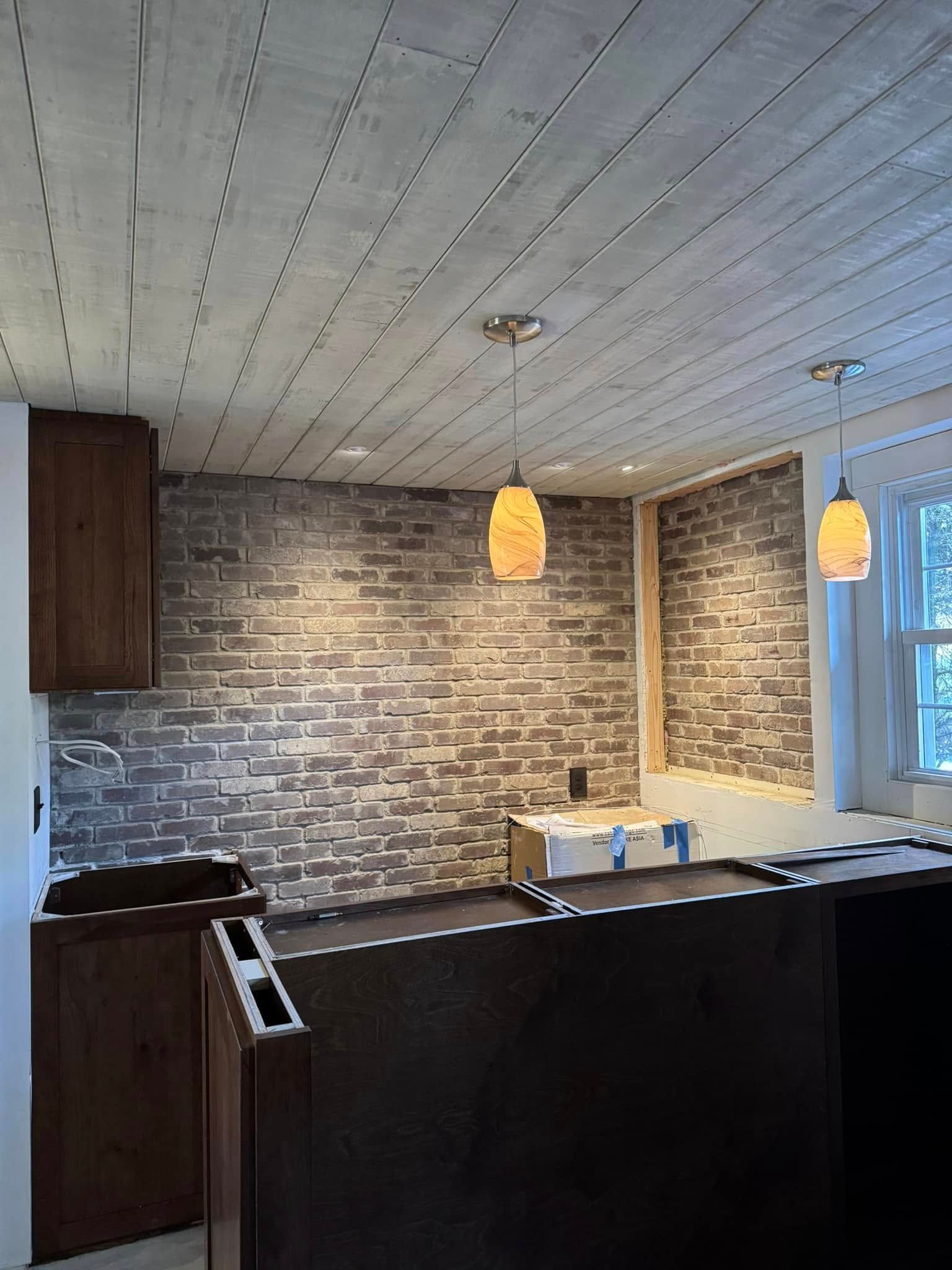 A kitchen with a brick wall and a wooden ceiling.