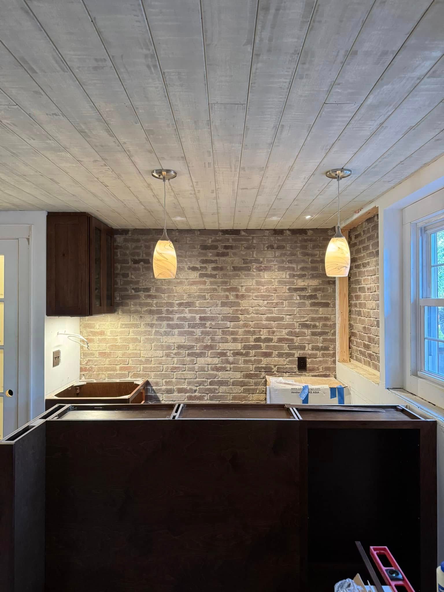 A kitchen with a wooden ceiling and a brick wall.