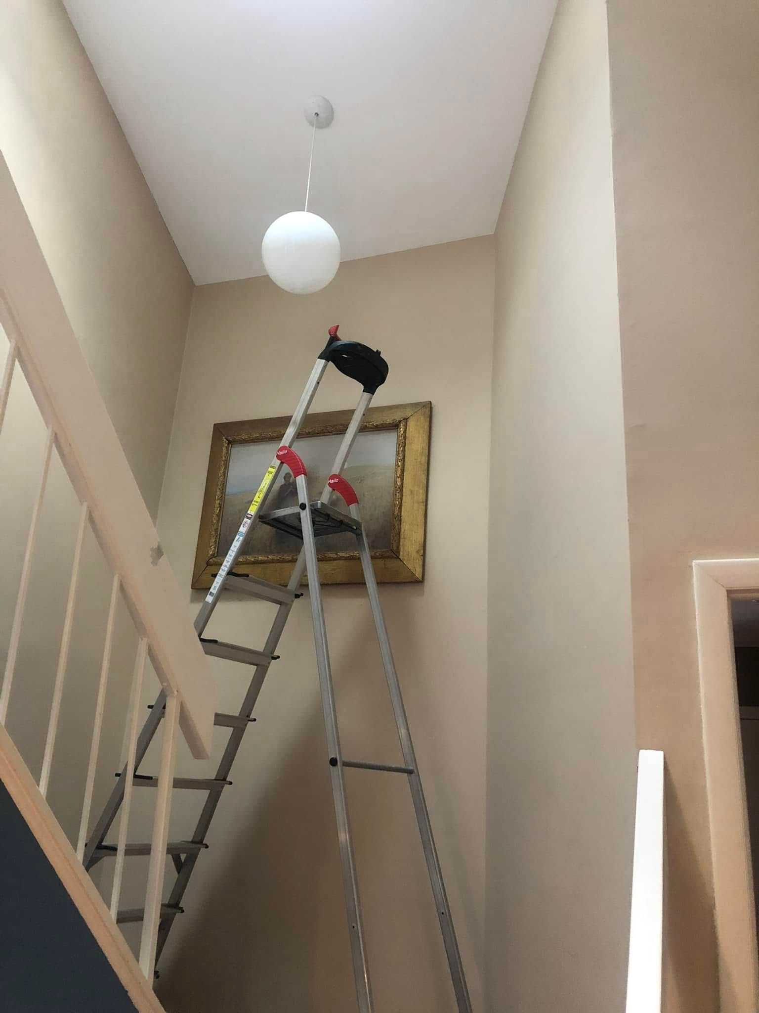 A ladder is sitting on top of a staircase next to a picture on the wall.