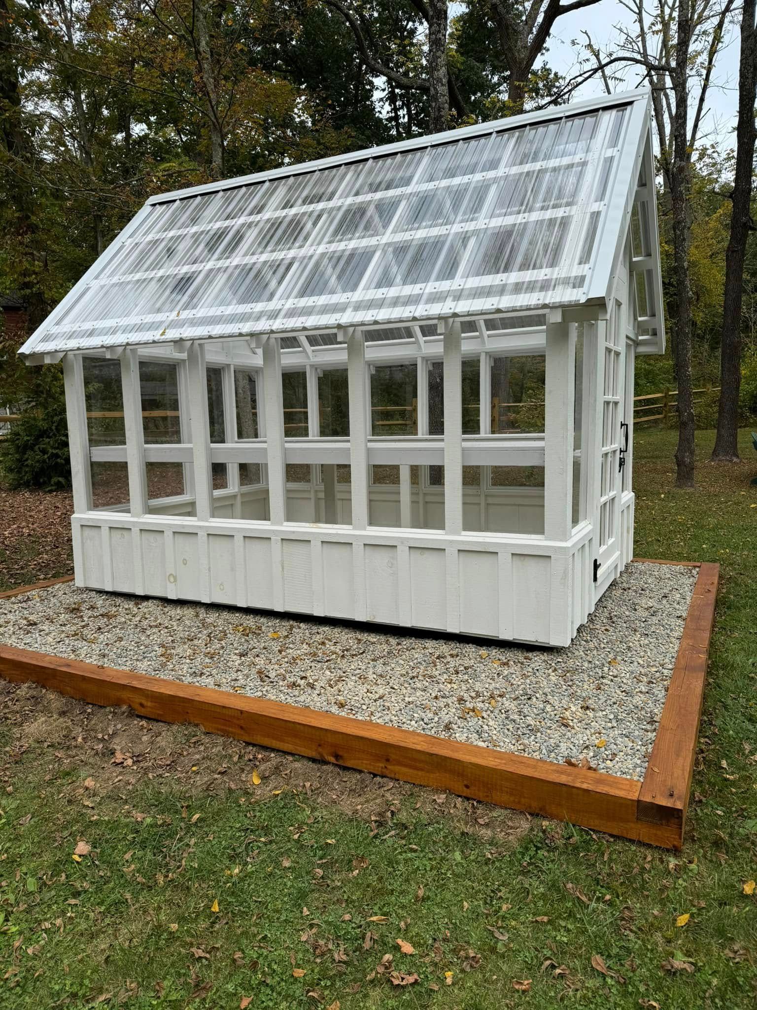 A white greenhouse with a clear roof is sitting on top of a gravel area.