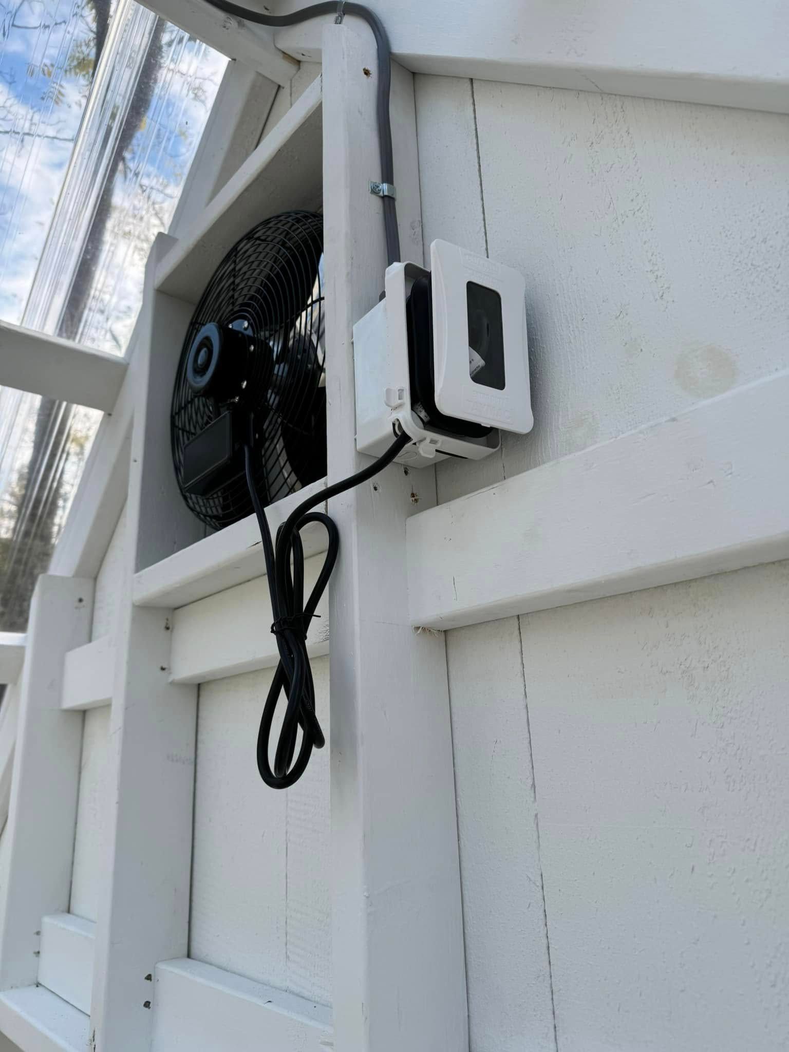 A fan is attached to the side of a white fence.