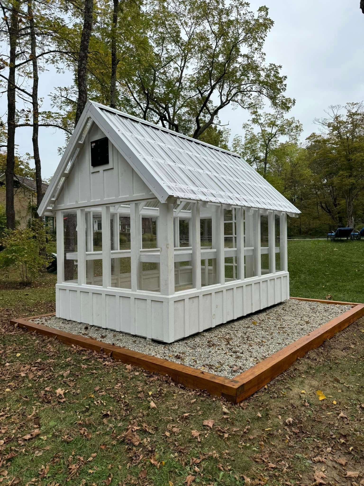 A white greenhouse with a metal roof is sitting in the middle of a grassy field.