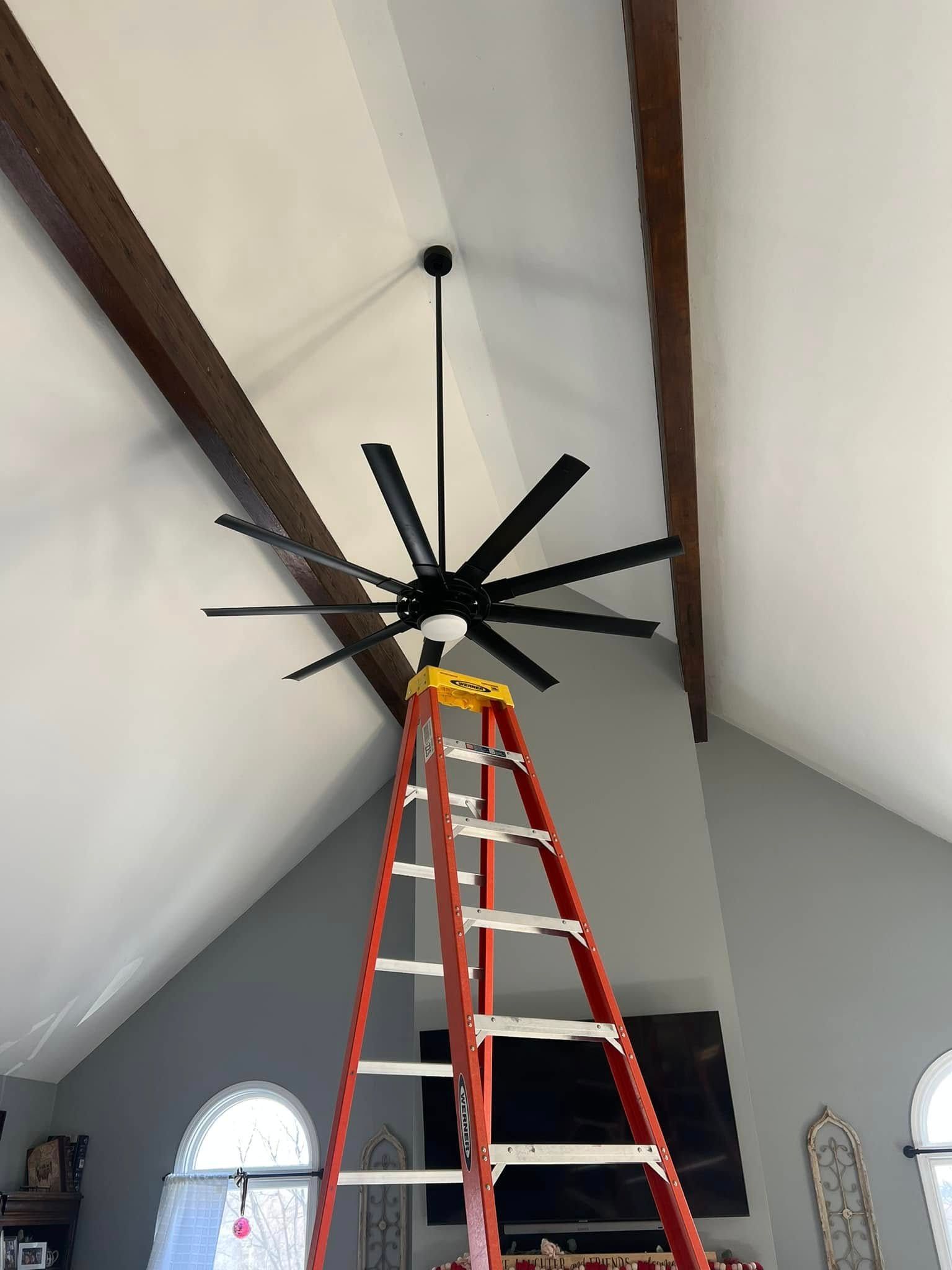 A ceiling fan is being installed in a living room with a ladder.