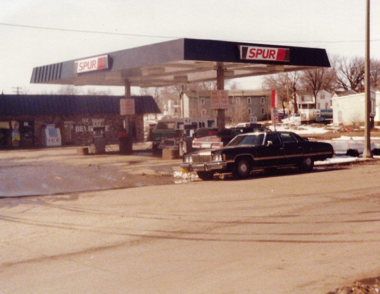 Spur gas station with black canopy, cars parked, and a dark sedan in front.