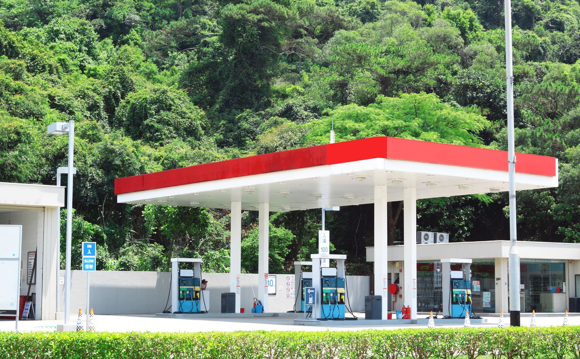 Gas station with red and white canopy, blue fuel pumps, lush green trees in the background.