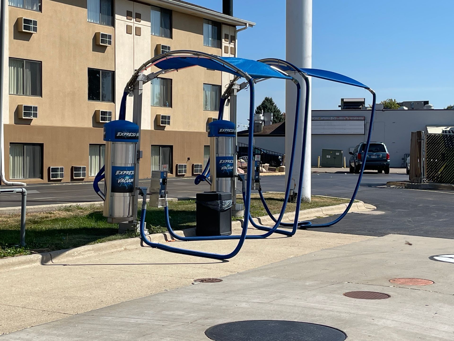 Blue and silver car vacuum station with overhead cover, outside of a building on a sunny day.