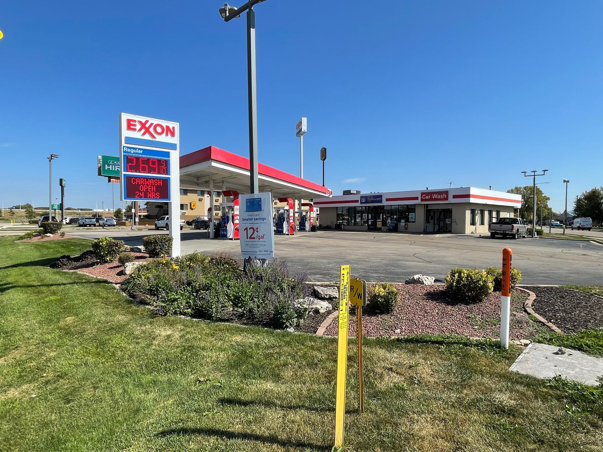 Exxon gas station with red and white canopy and prices displayed, sunny day.