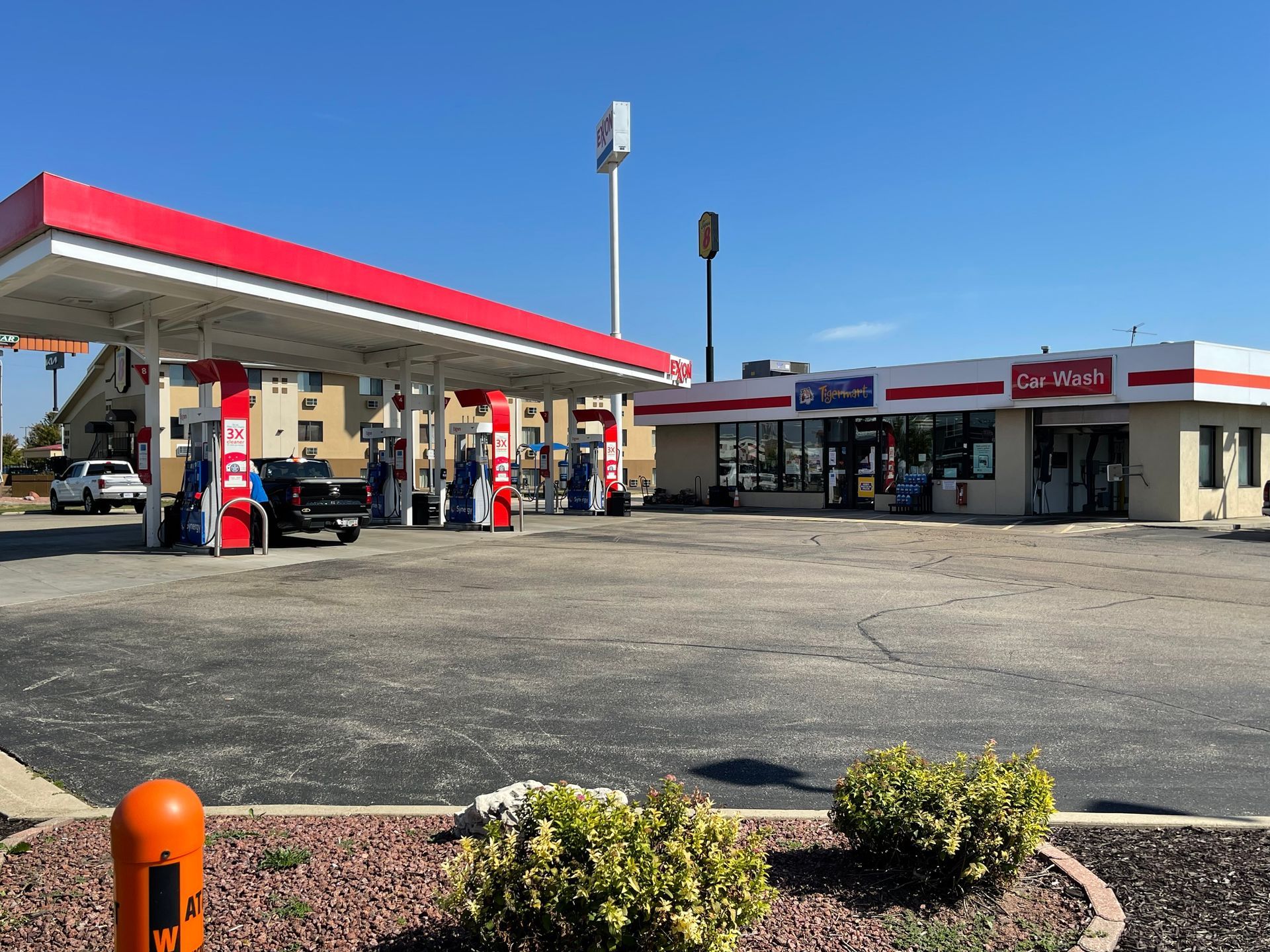 Gas station with red canopy, pumps, and convenience store under a clear blue sky.