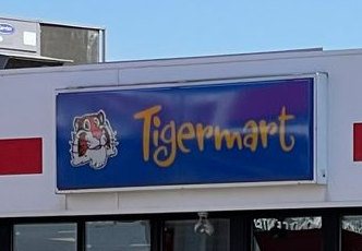 Tigermart store sign with cartoon tiger logo and gold lettering on a blue background.