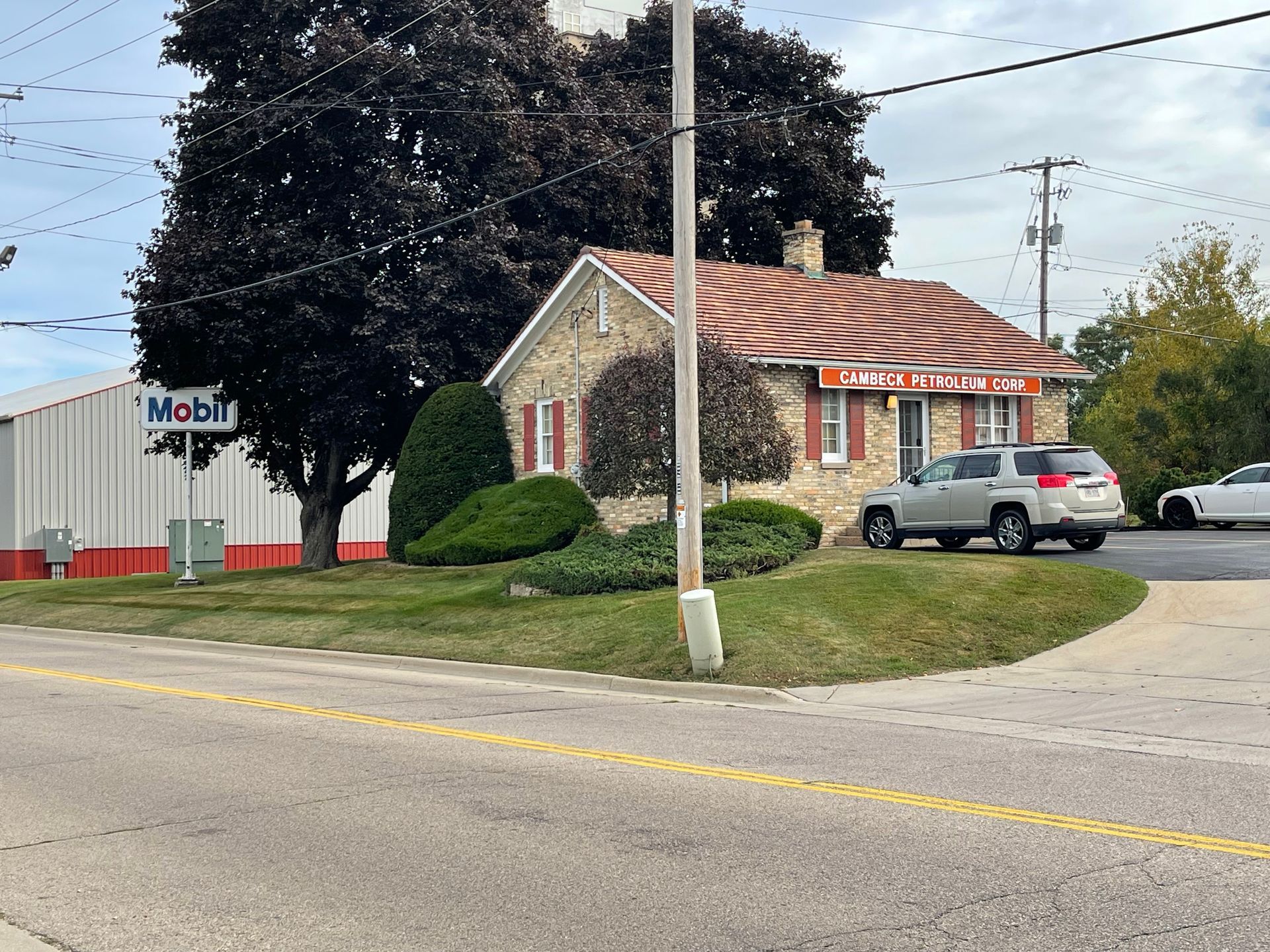 A small stone building with a red-tiled roof and a Mobil gas station sign, beside a street.