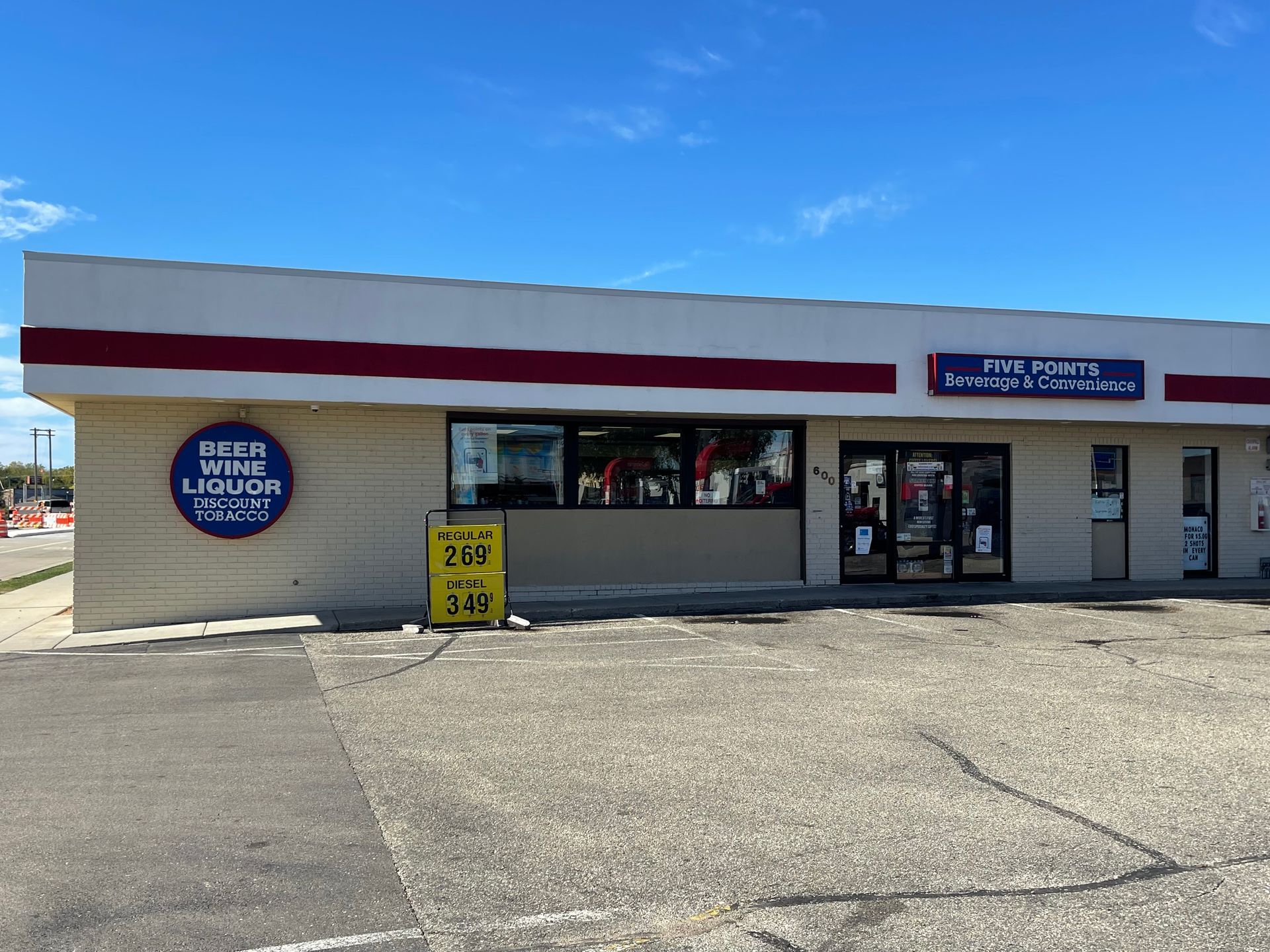 Exterior of a liquor store with a blue and white facade under a bright sky. A sale sign is in front.