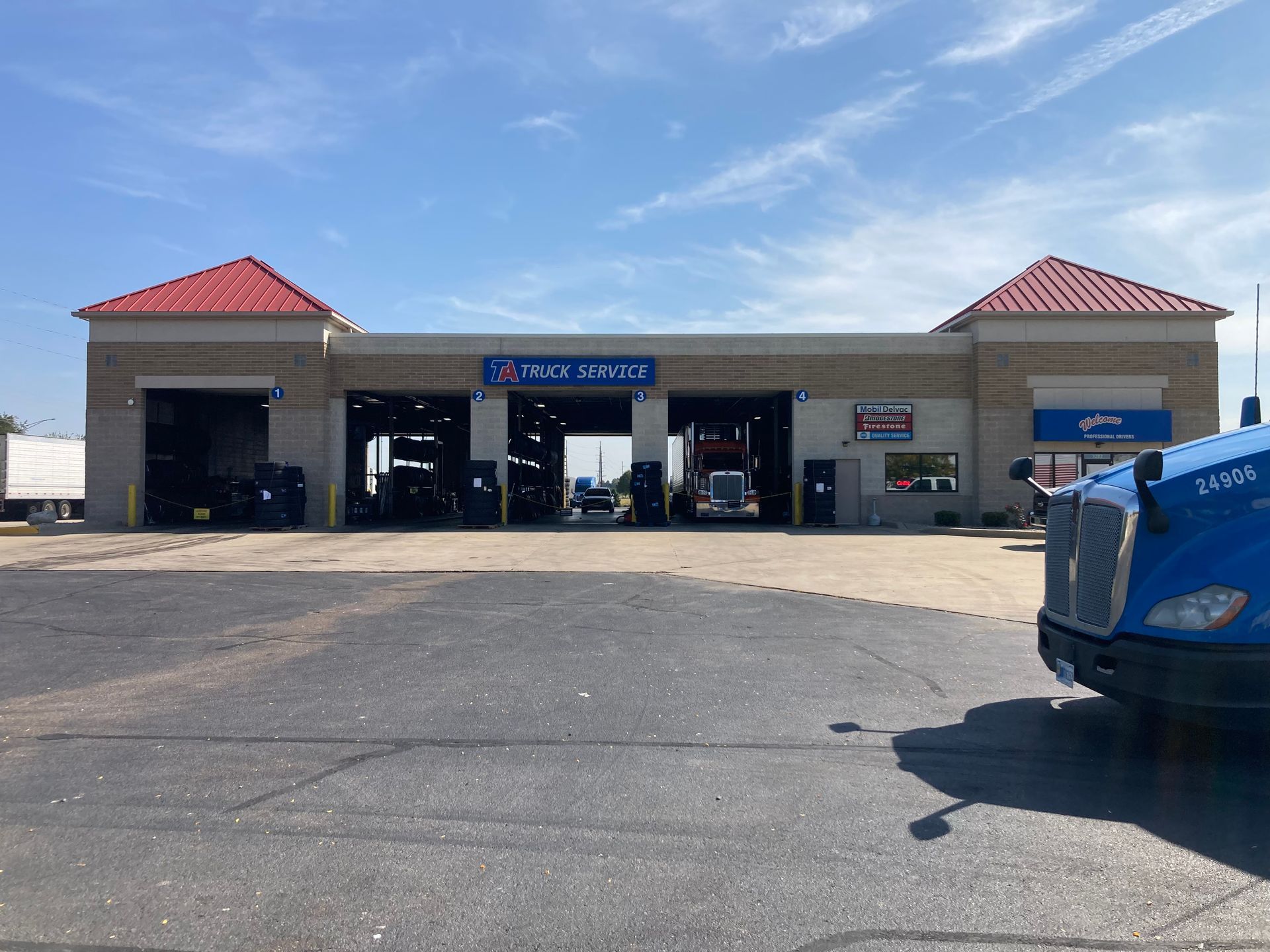 A truck service center with open bays; a blue semi-truck is parked in the foreground under a blue sky.