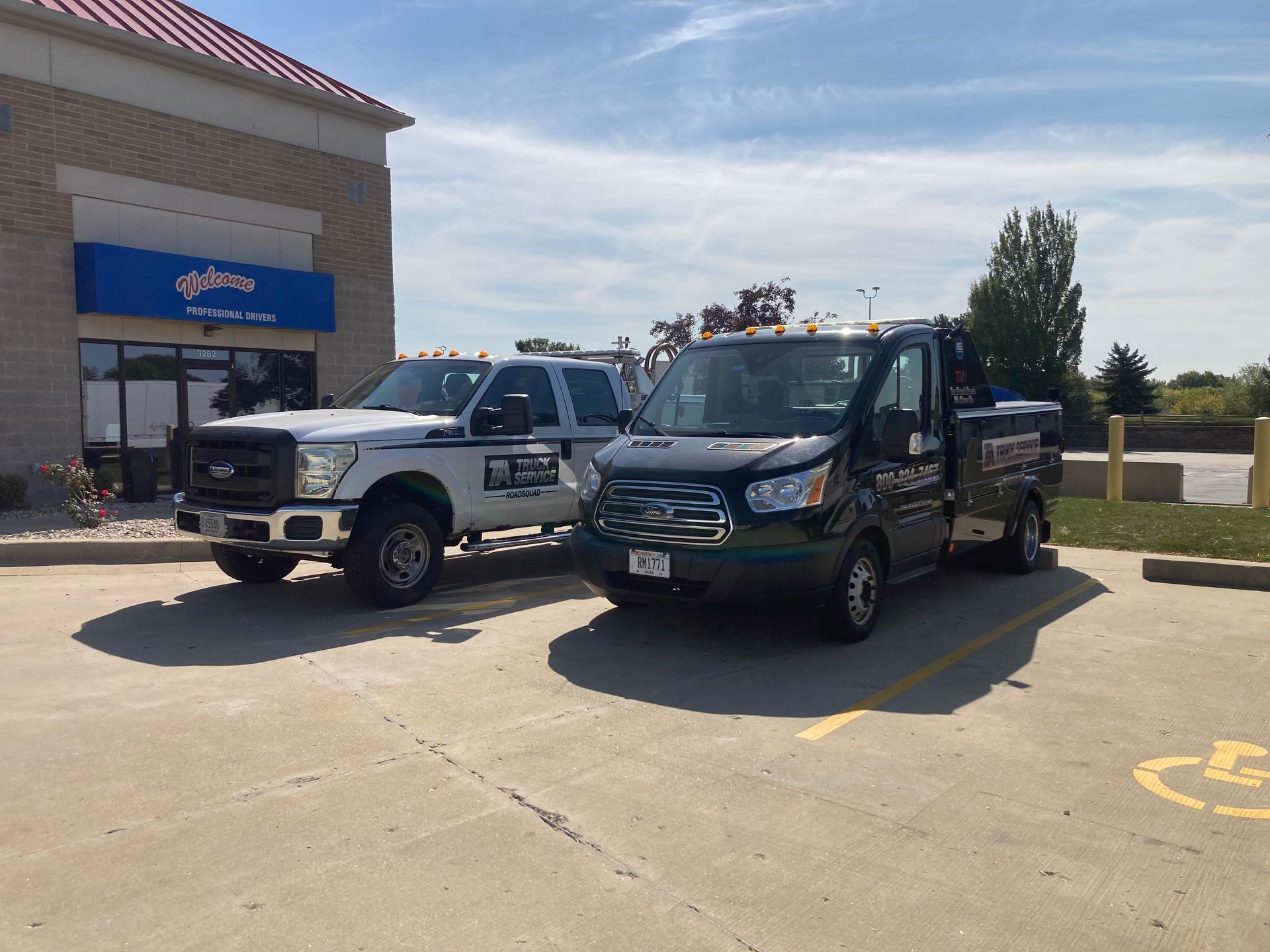 Two work trucks parked outside a building with a blue awning.