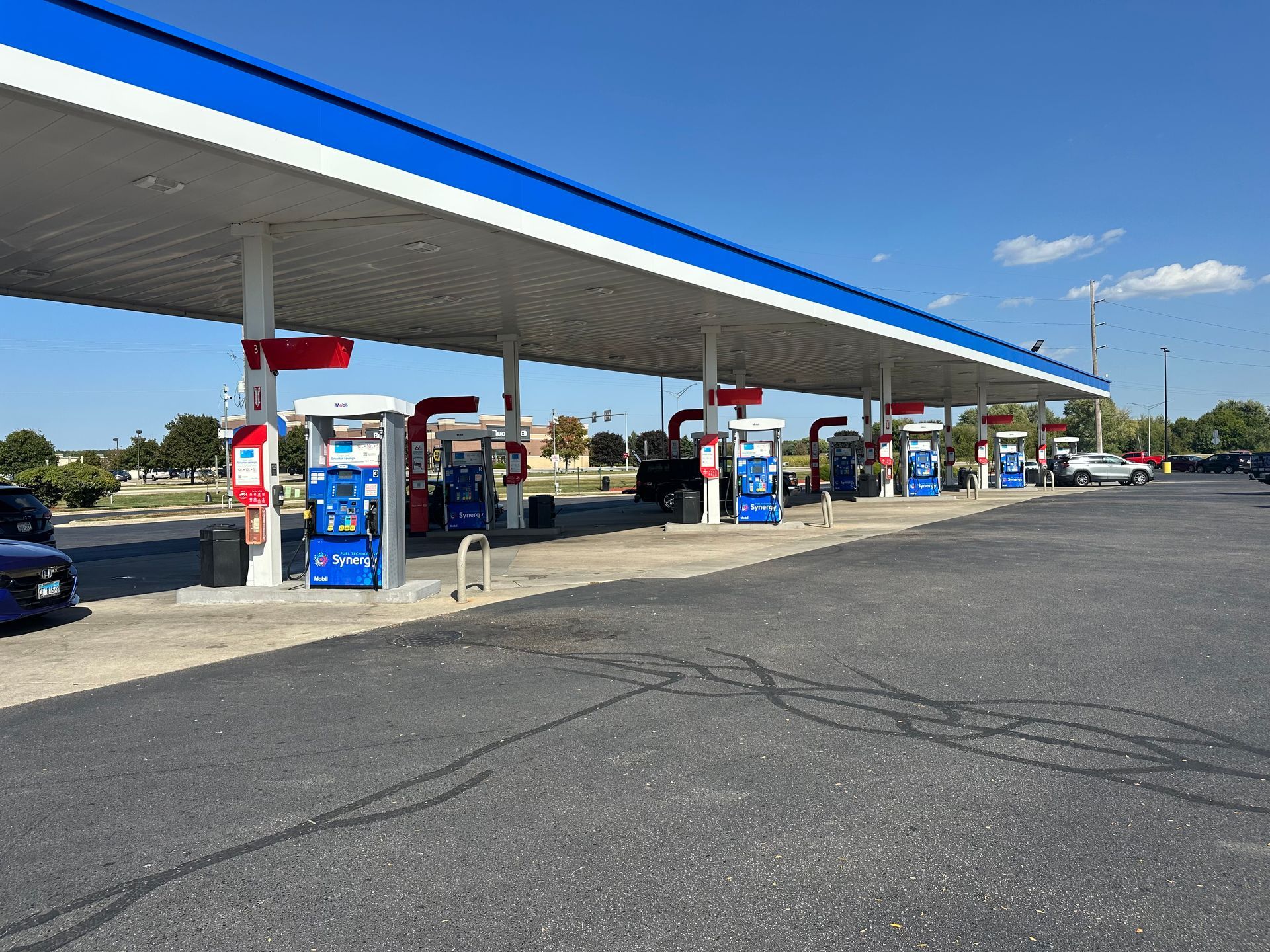 Gas station with multiple pumps under a white and blue canopy on a sunny day.